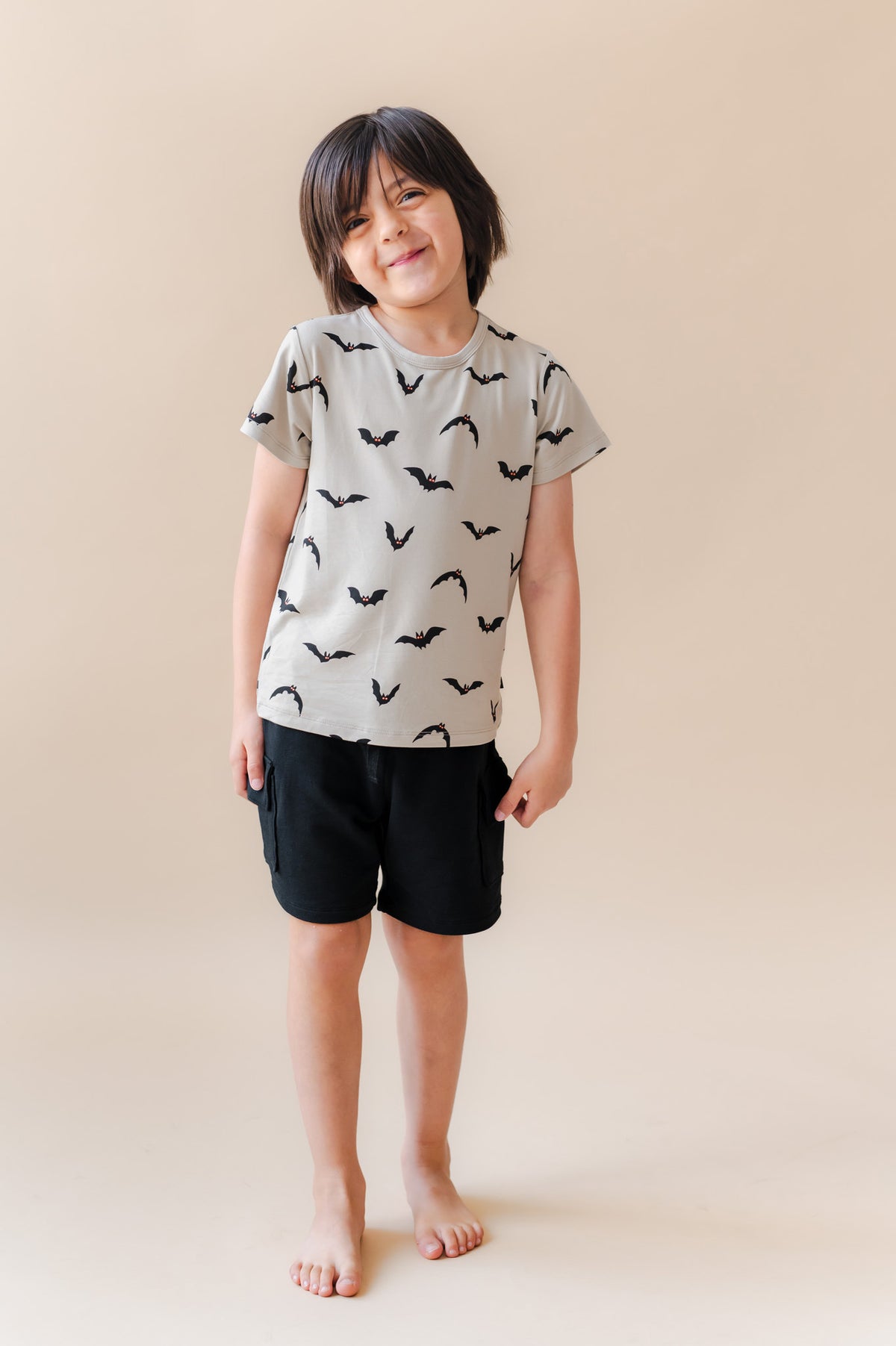 Boy posing in Toddler Basic Tee in Bats print over black shorts on a beige background