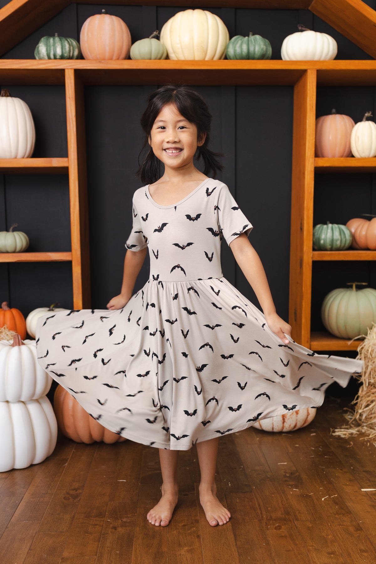 Girl in Twirl Dress in Bats print smiling in front of pumpkin decorations