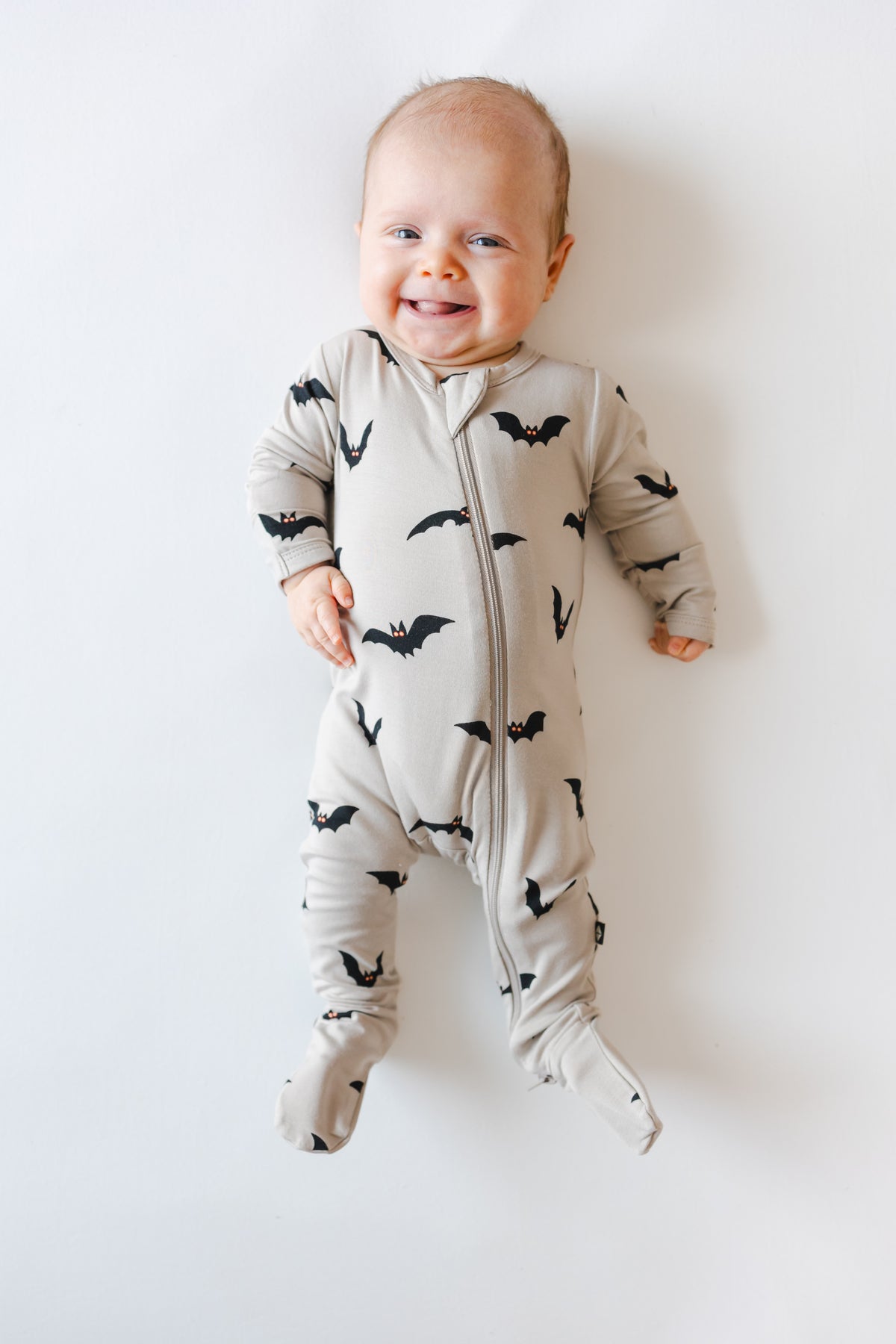 Baby smiling in Zippered Footie in Bats print on a white background