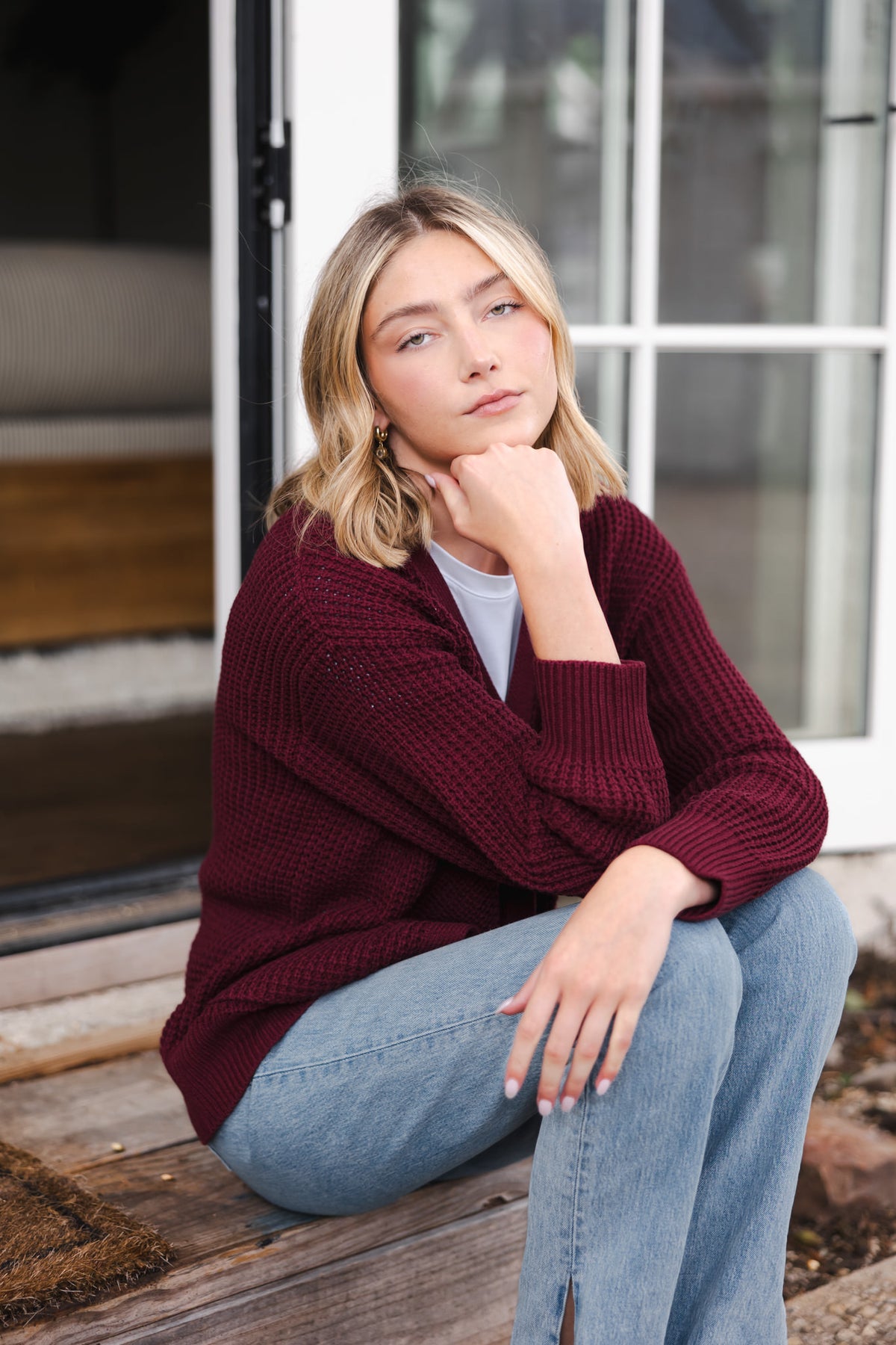 Modal posing outdoors wearing Chunky Knit Women's Waffle Cardigan in Burgundy over white T-shirt and blue jeans