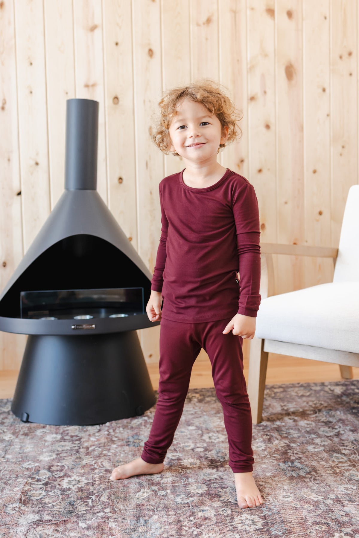 A young child wearing a matching burgundy long-sleeve top and pant pajama set