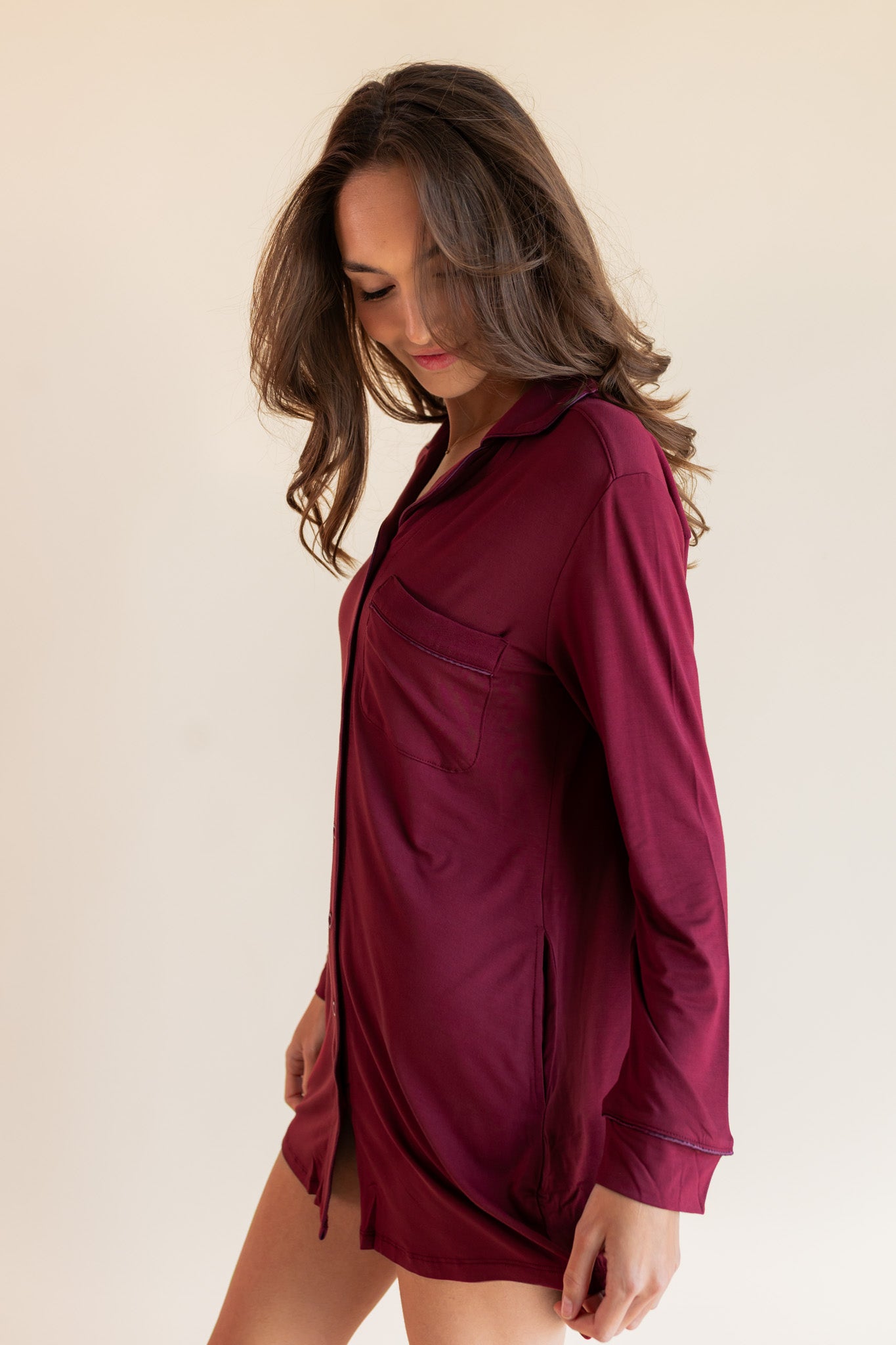 A woman wearing a long-sleeve burgundy button-up shirt dress, photographed against a solid light beige background.