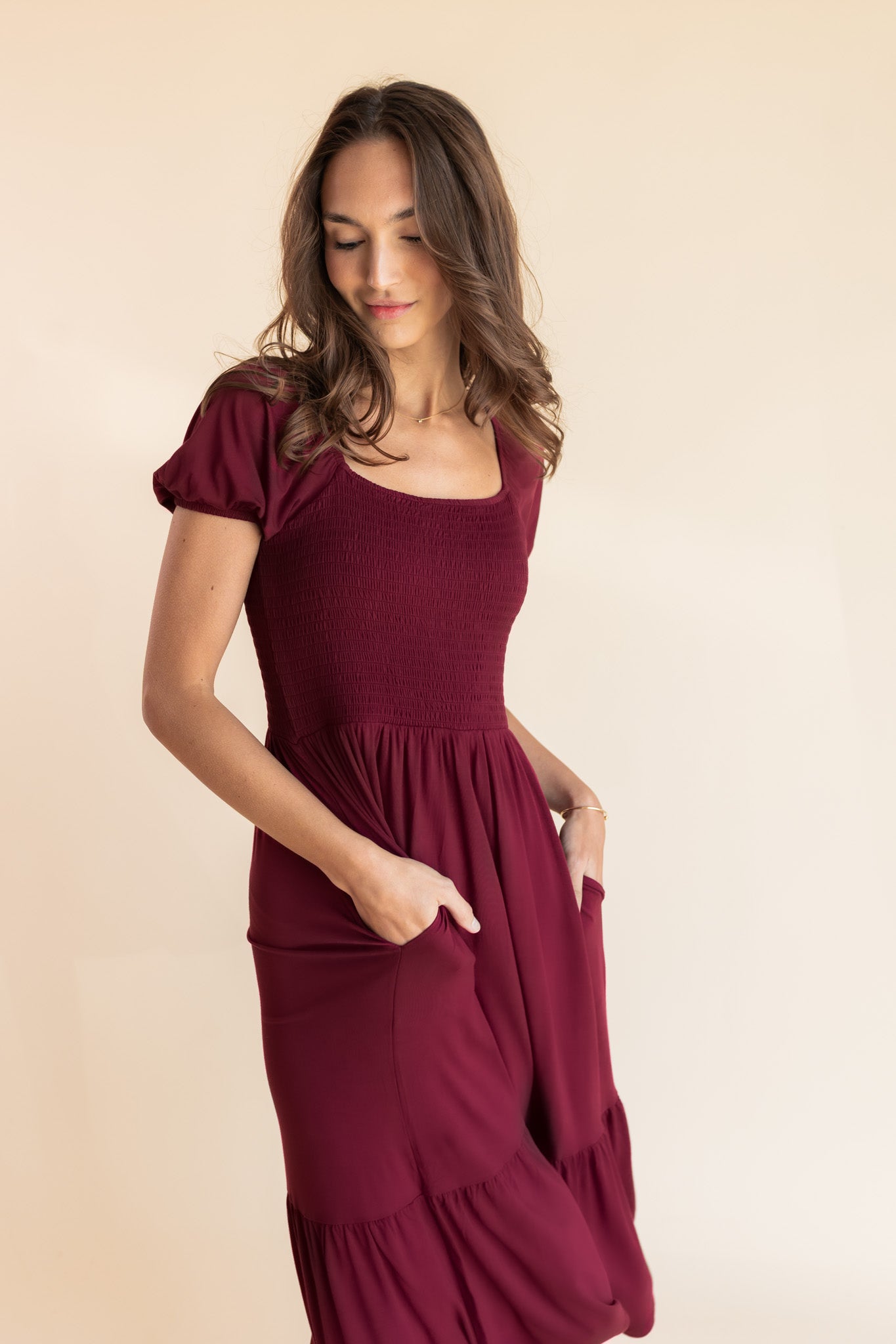 Model posing in Women’s Smocked Dress in Burgundy with pockets on a beige background