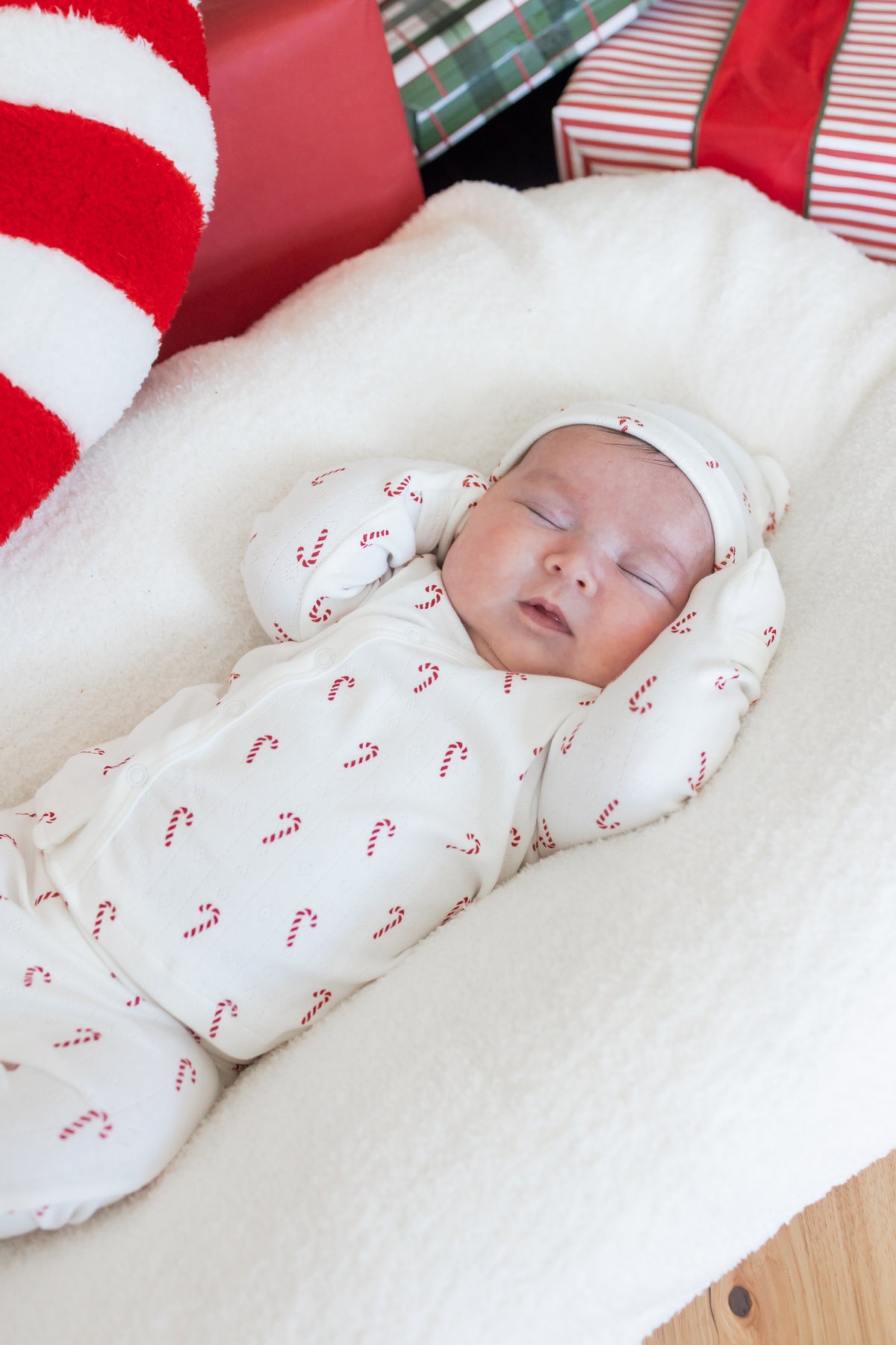 Close up of Baby sleeping wearing Pointelle Take Me Home Set with Cap in Candy Cane print on a white crib sheet