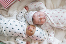 2 newborn babies sleeping wearing pointelle take me home sets in delicate christmas patterns laying near christmas presents 