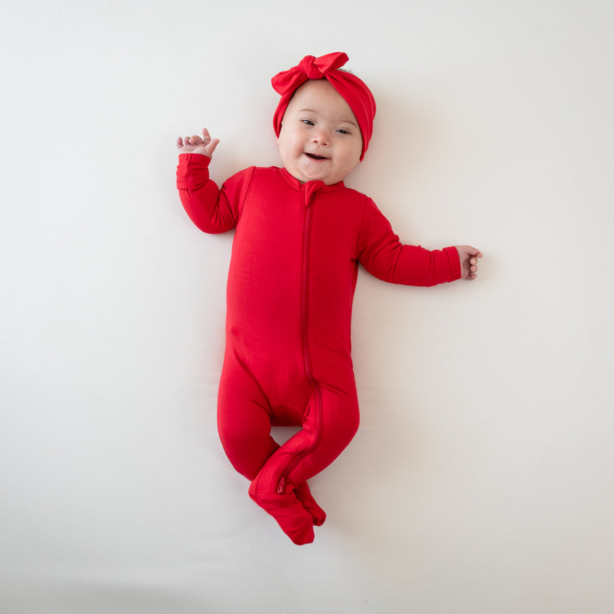 Baby modeling Zippered Footie in Cardinal with matching bow