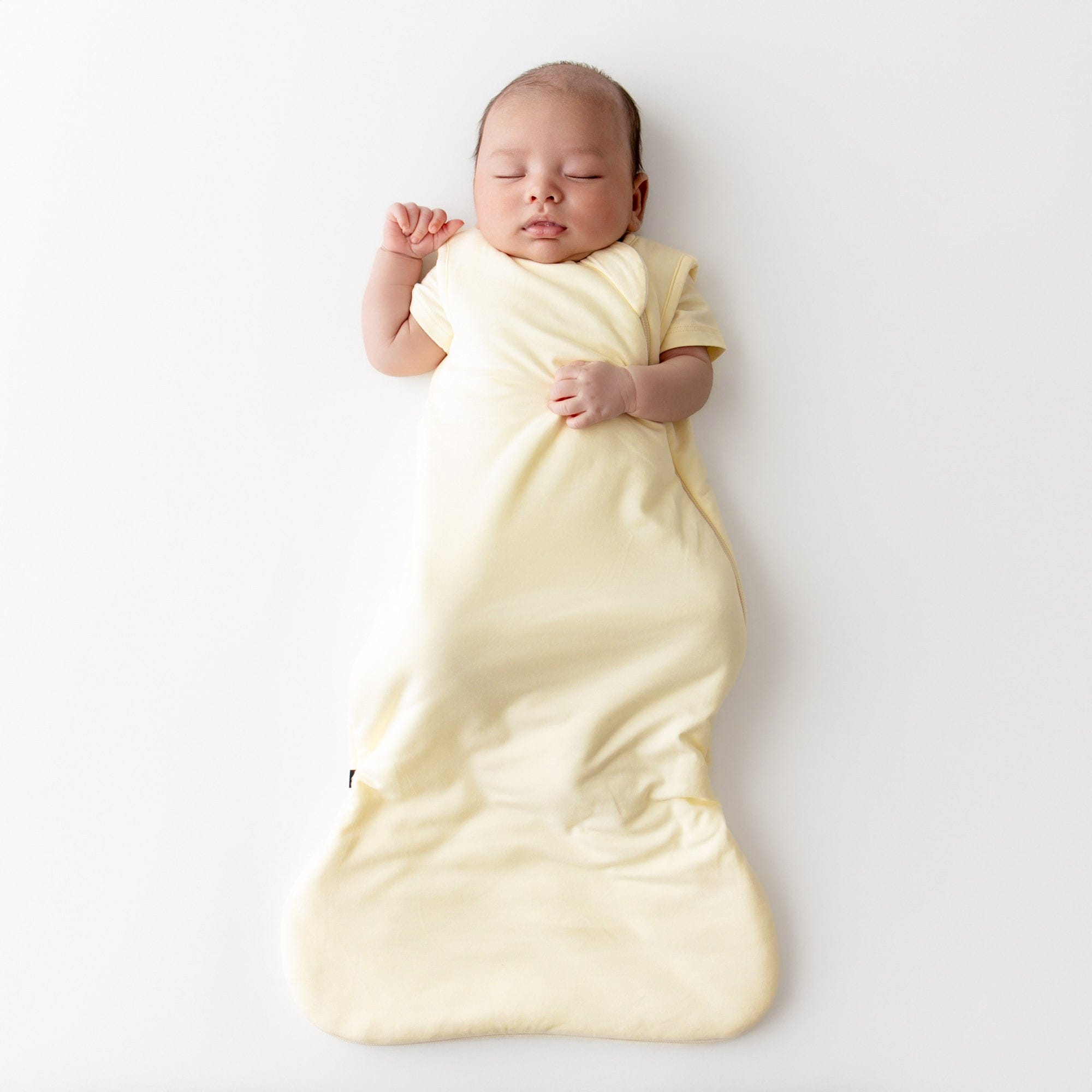 Baby asleep wearing a kyte baby sleep sack in a pale yellow color