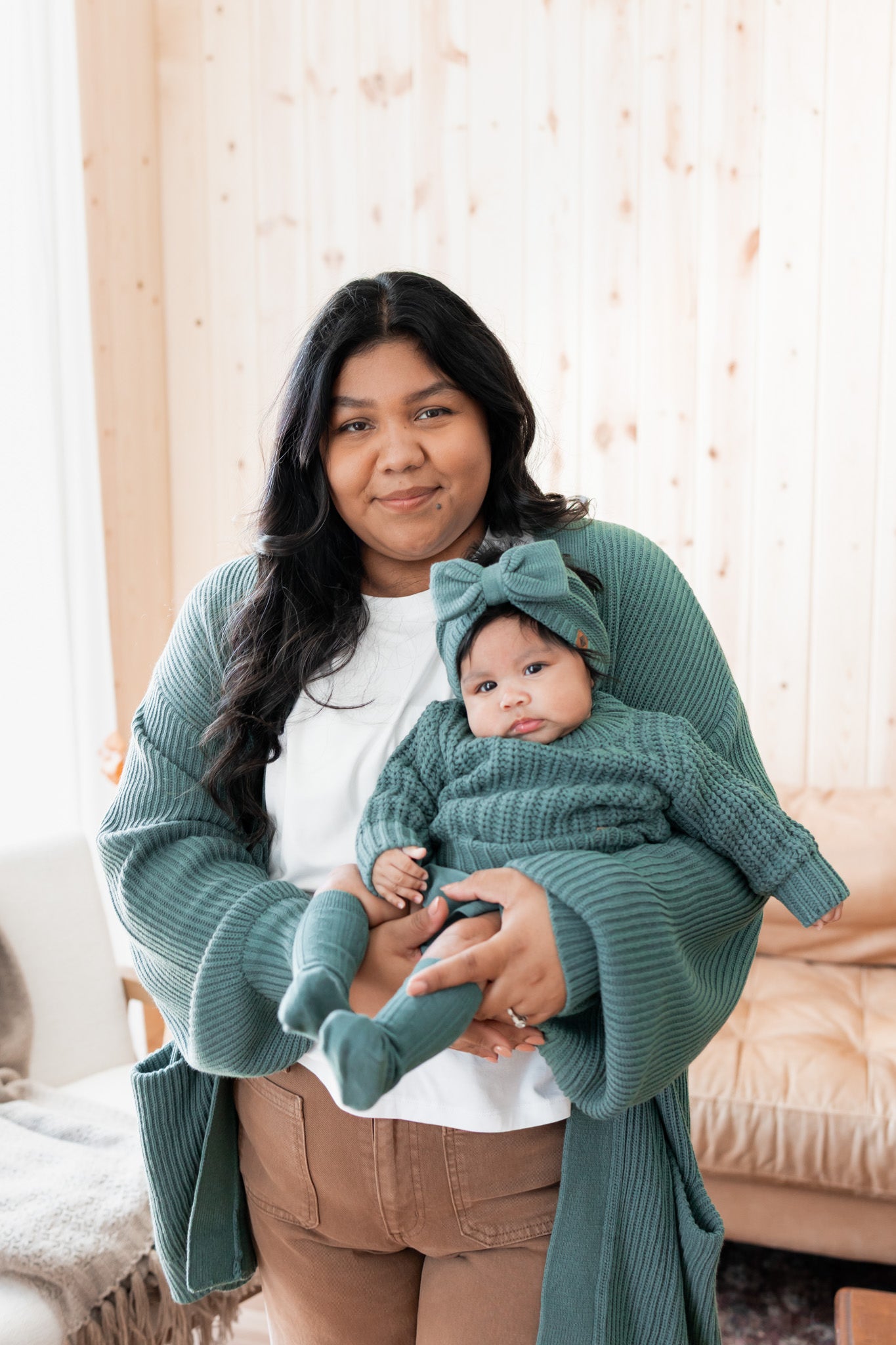 Modal wearing Chunky Knit Women's Oversized Cardigan in Pine holding baby wearing Chunky knit sweater, chunky knit bow headband and socks in pine