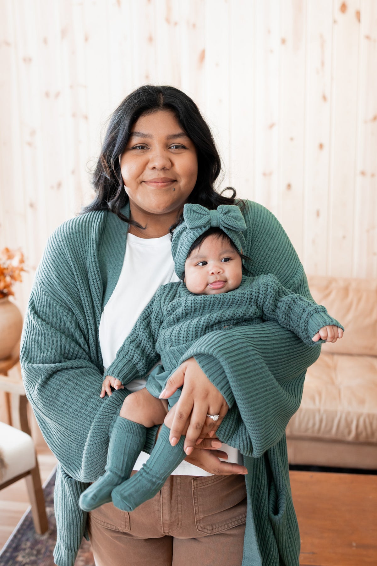 Modal wearing Chunky Knit Women's Oversized Cardigan in Pine holding baby wearing Chunky knit sweater, chunky knit bow headband and socks in pine