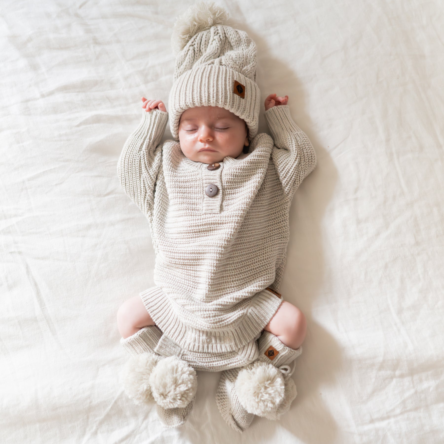 Sleeping newborn wearing the Chunky Knit Romper in Oat and matching knit booties and Chunky Cable Knit Beanie