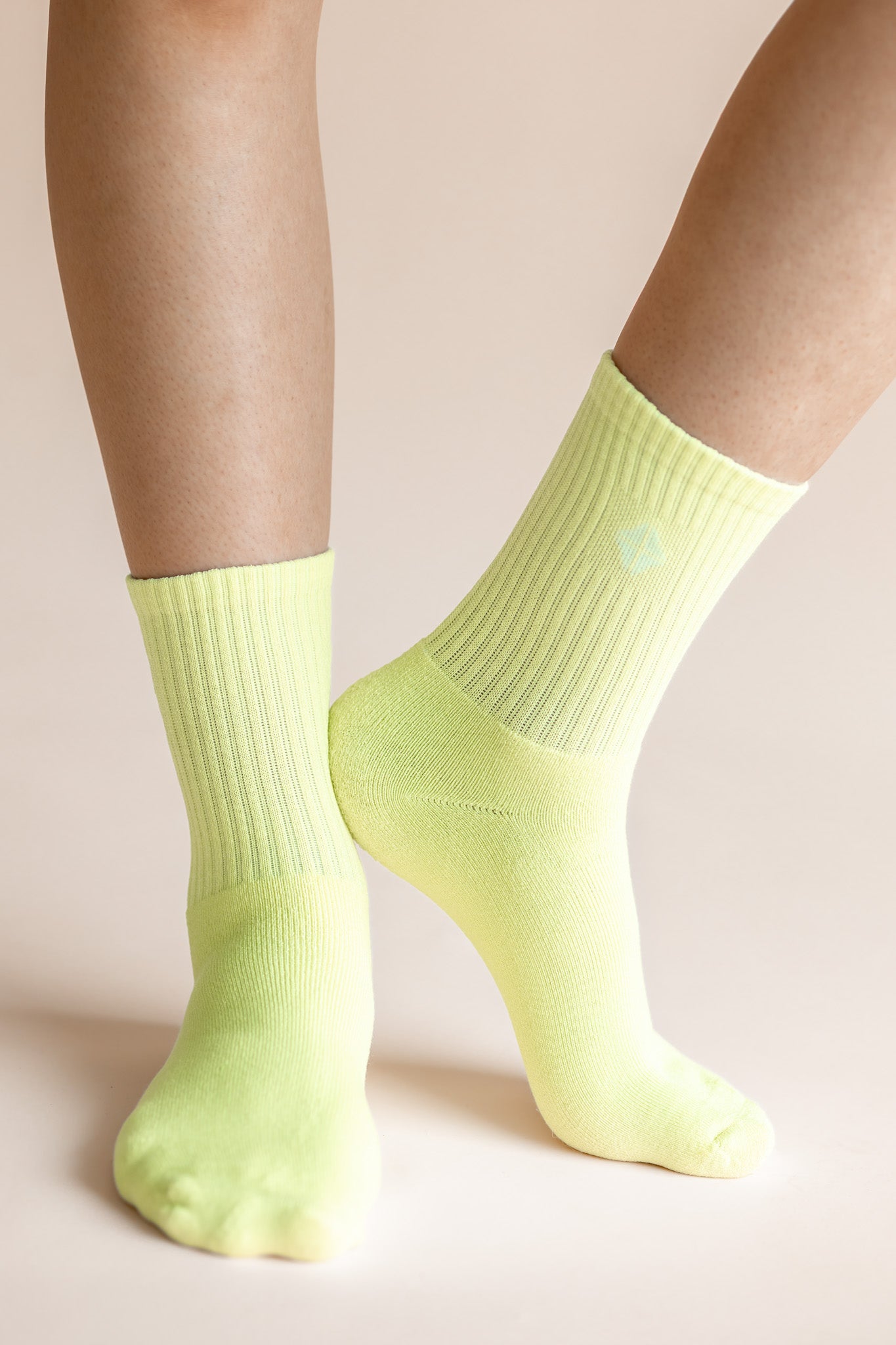 A close-up of a person's feet and lower legs wearing bright neon yellow-green crew socks against a solid pale beige background.