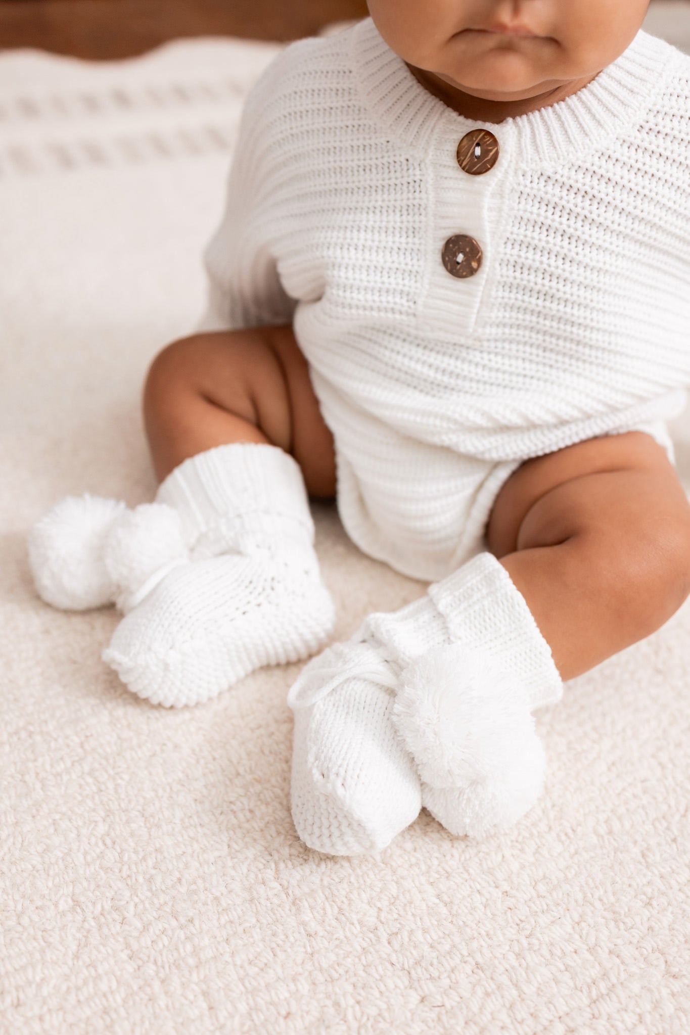 Baby sitting on a white carpet wearing Chunky Knit Romper and knit booties in cloud