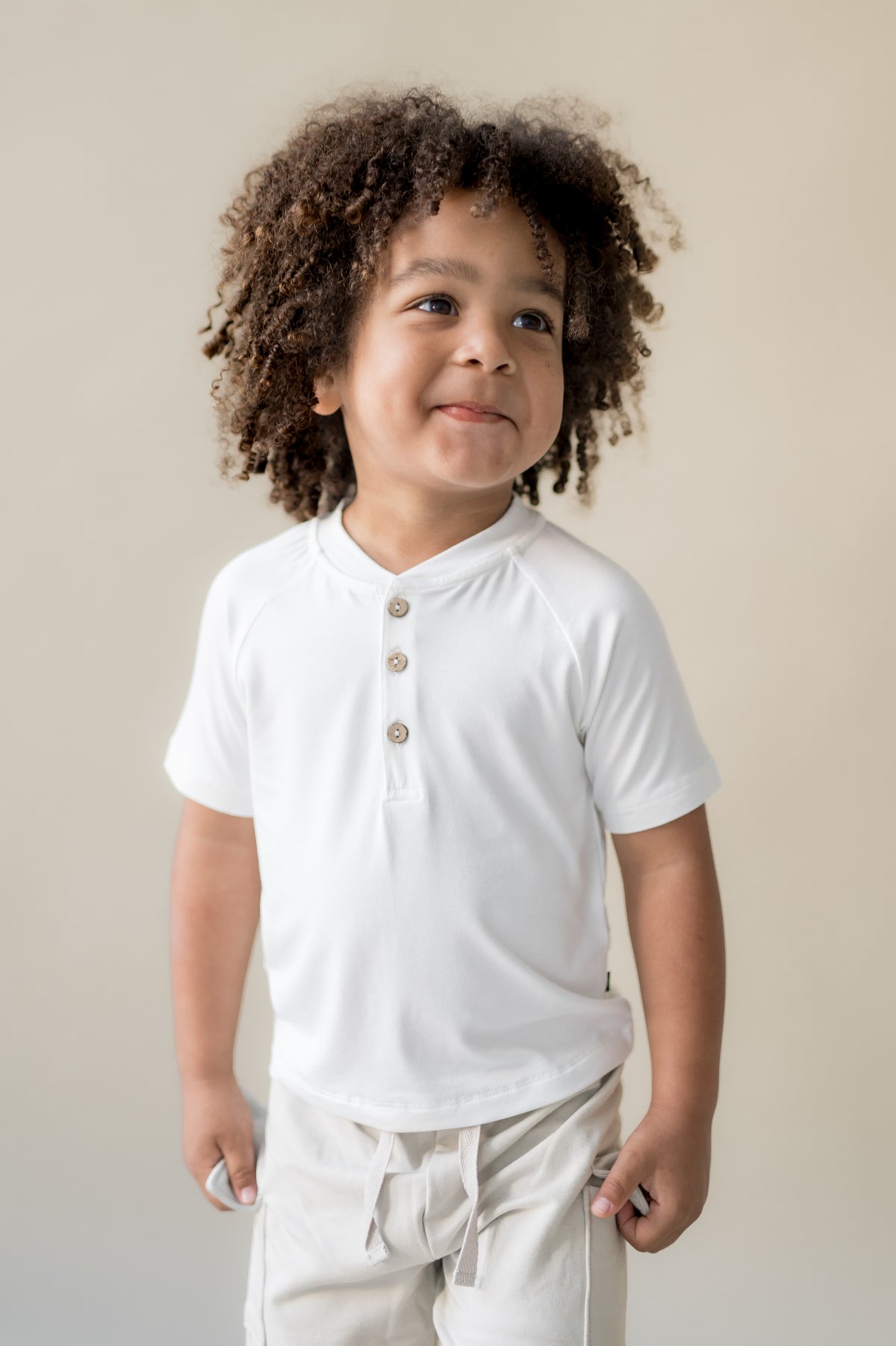 Young boy wearing the Short Sleeve Toddler Henley Tee in Cloud paired with the oat cargo shorts
