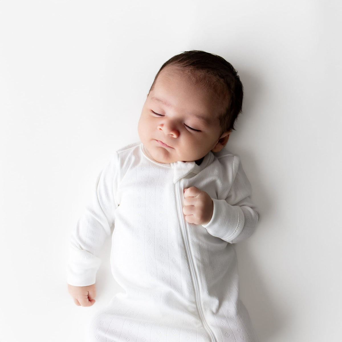 Close up a sleeping newborn wearing the Pointelle Zippered Footie in Cloud