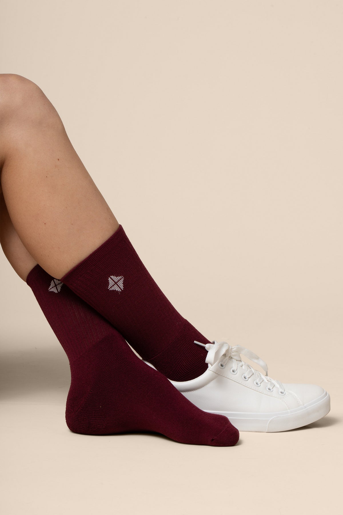 Maroon socks with a logo worn by a person on a beige background