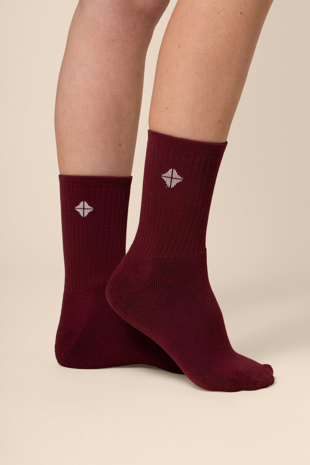 Maroon socks with a logo worn by a person on a beige background