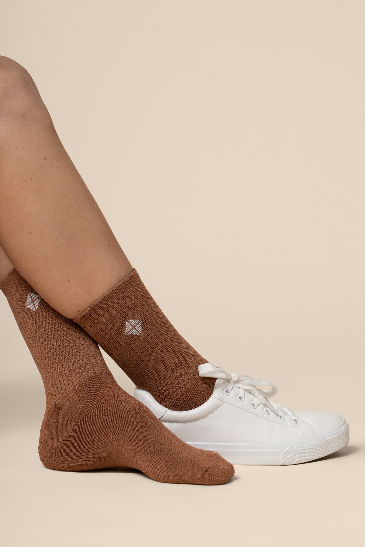 Brown socks worn with white sneakers on a beige background