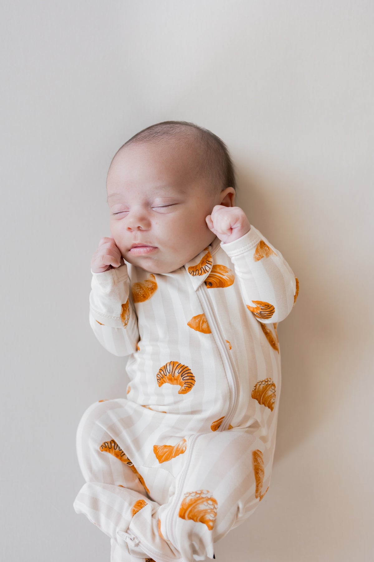 Baby sleeping in Zippered Footie with Croissant print on a beige background