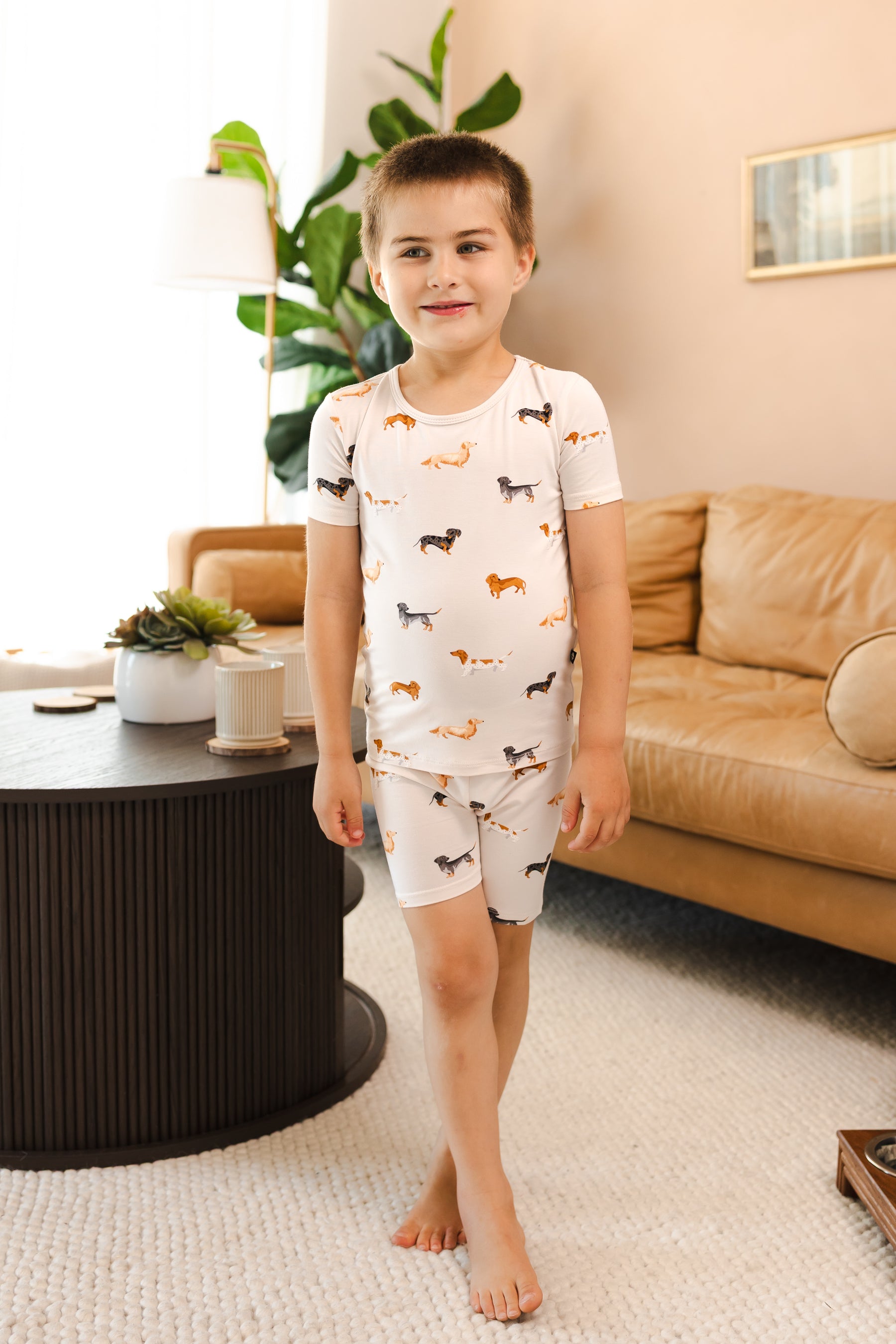 Boy standing in Beige Short Sleeve Pajamas in Dachshund print in a living room 