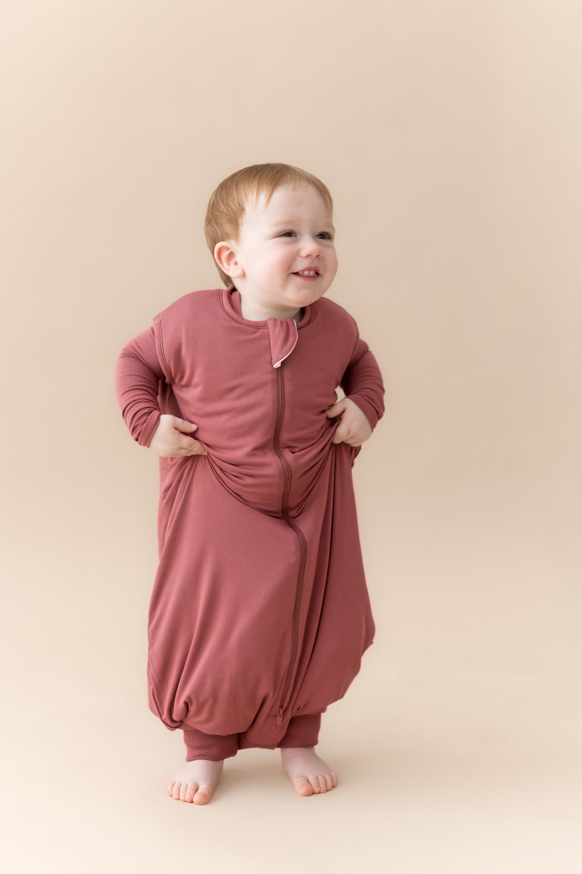 Child posing in Sleep Bag Walker in Ember 1.0 on a beige background