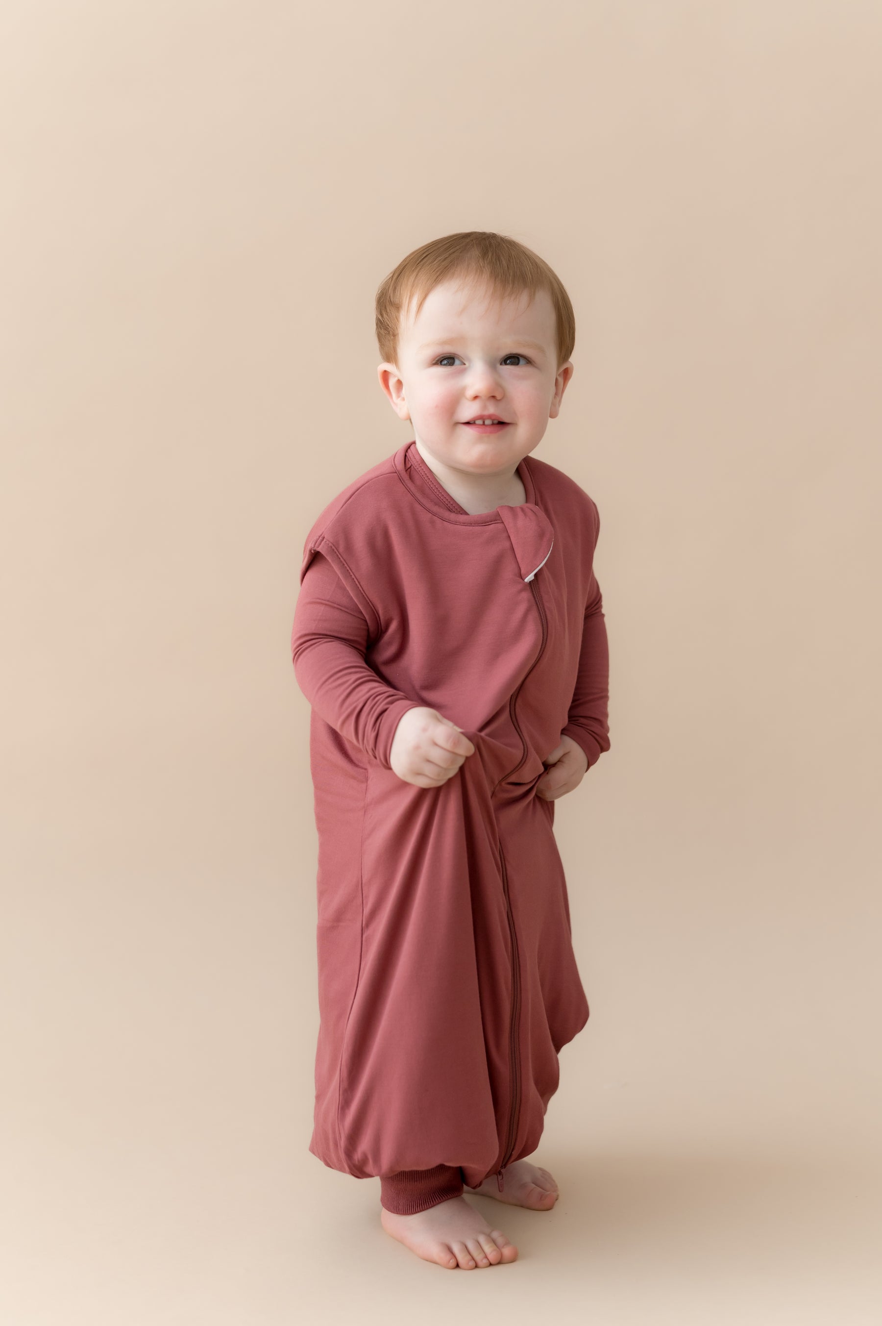 Child standing wearing Sleep Bag Walker in Ember 1.0 on a beige background