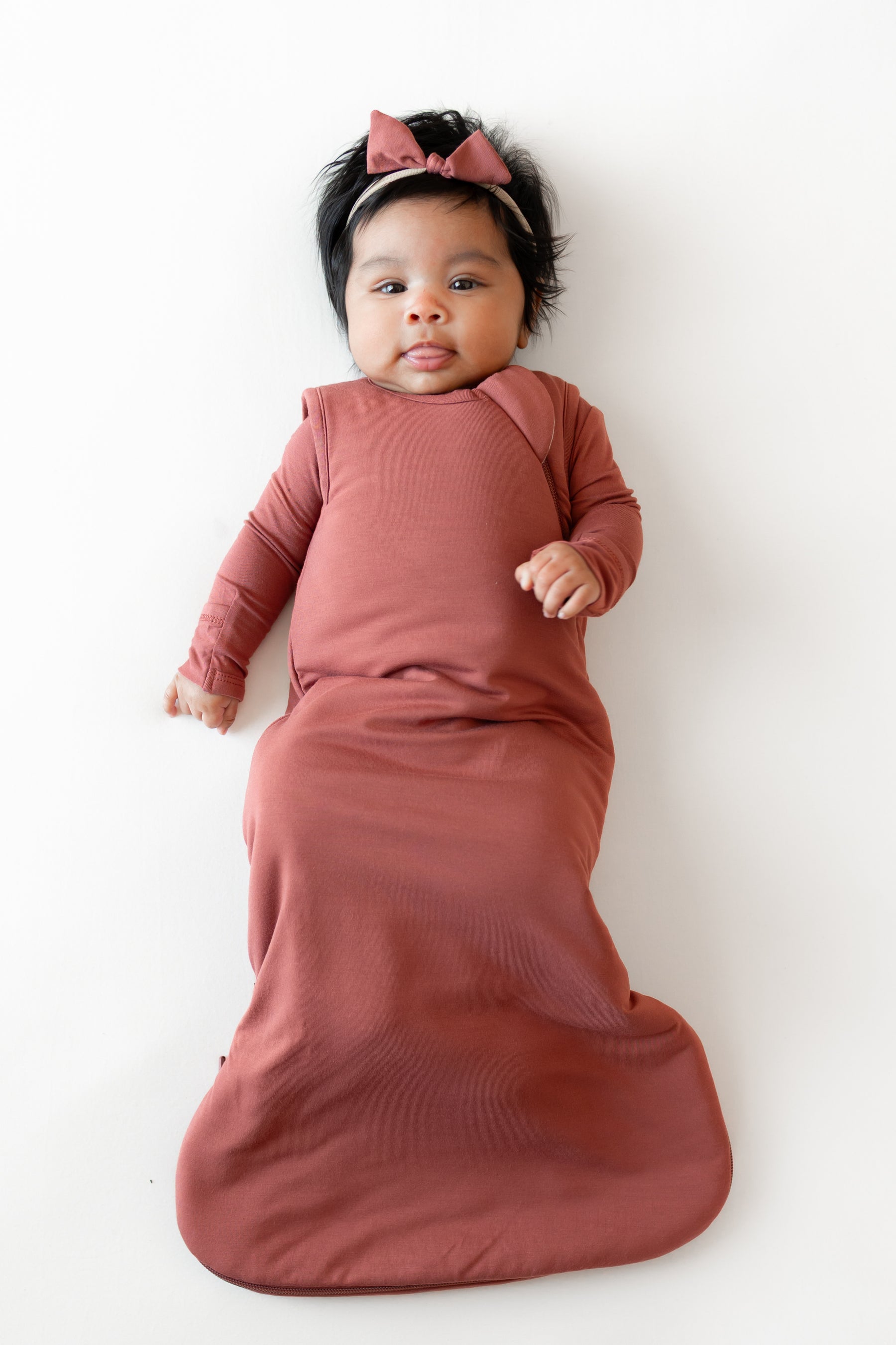 Baby wearing Sleep Bag and Bow headband in Ember 1.0 on a white background
