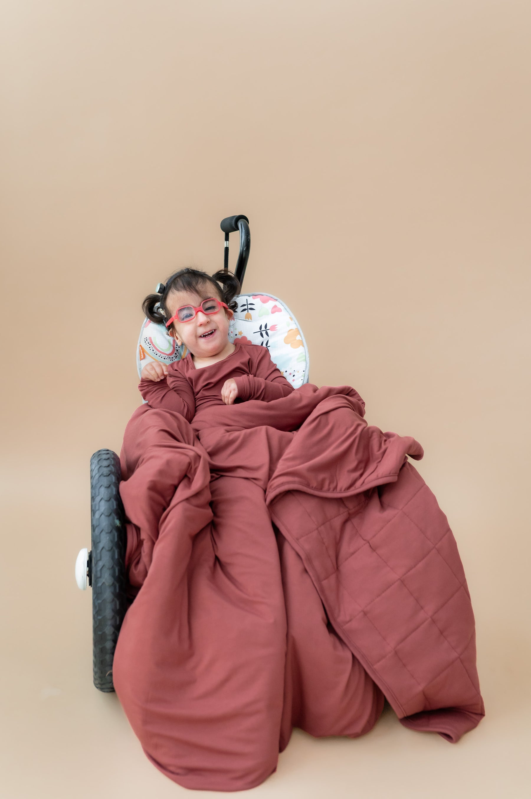 Child sitting on a wheel chair wrapped in Toddler Blanket in Ember 2.5 wearing a similar color long sleeve pajamas