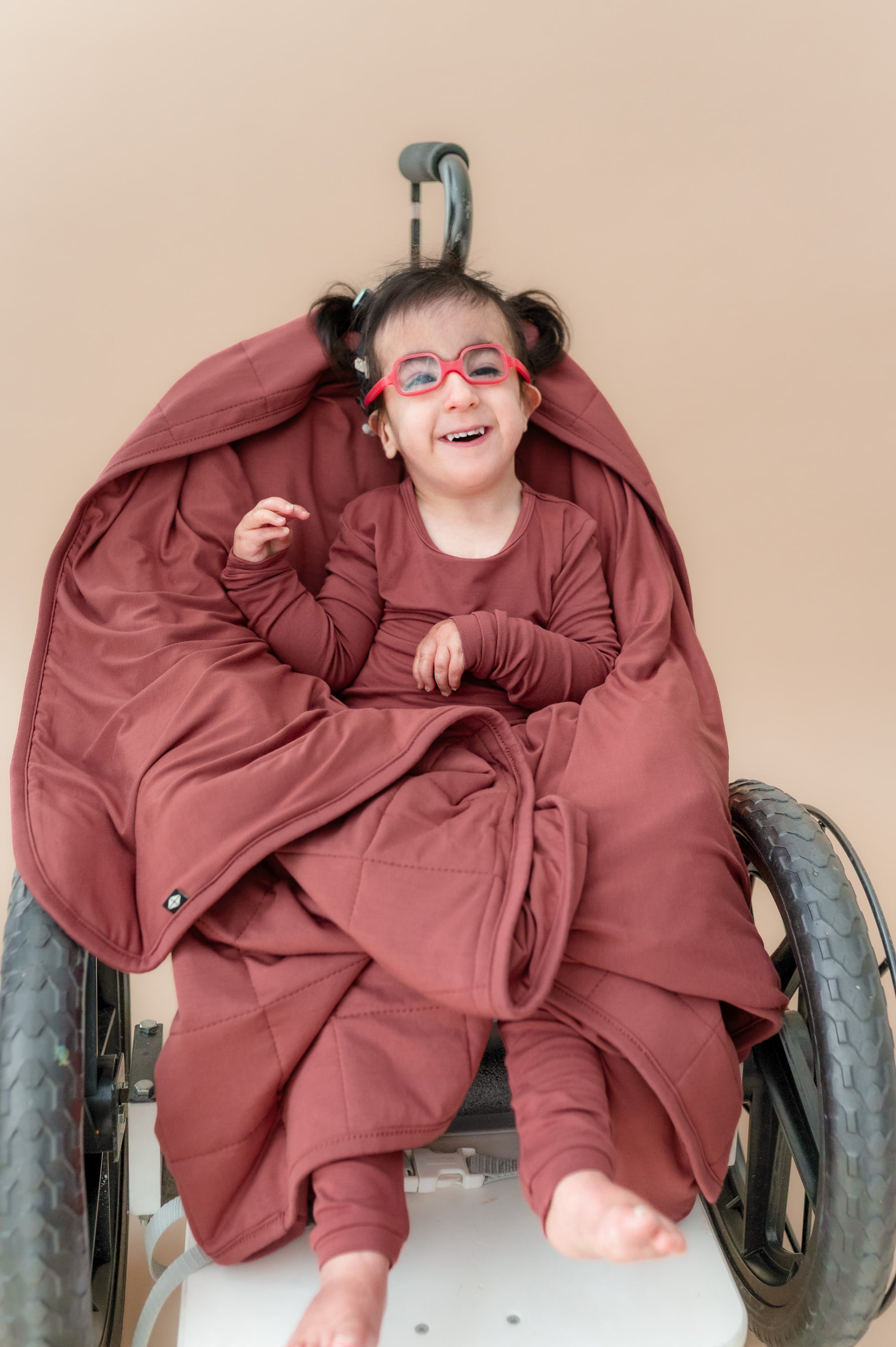 Child sitting on a wheel chair wrapped in Toddler Blanket in Ember 2.5 wearing a similar color long sleeve pajamas