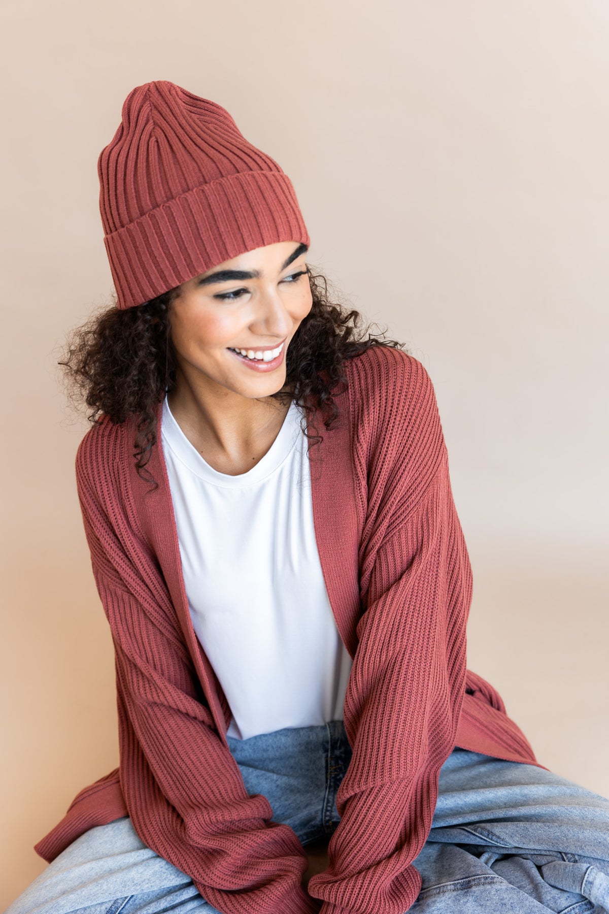 Modal wearing Chunky Knit Adult Ribbed Beanie in Ember over white T-shirt and Chunky knit cardigan in ember on a beige background