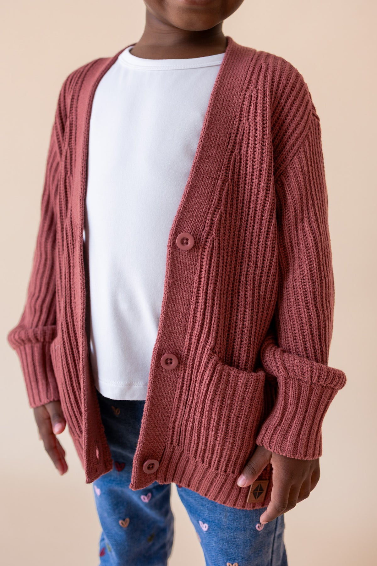 close up of Girl wearing Chunky Knit Oversized Cardigan in Ember over White T-shirt and blue jeans on a beige background