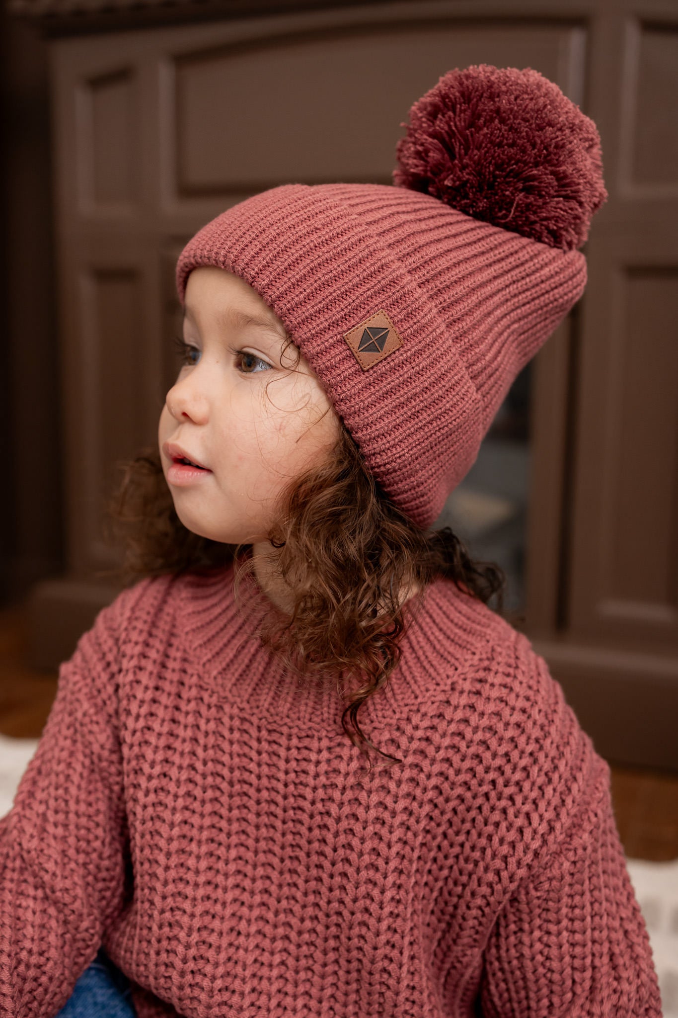 Girl wearing Chunky Knit Pom Beanie in Ember over Chunky knit sweater in ember
