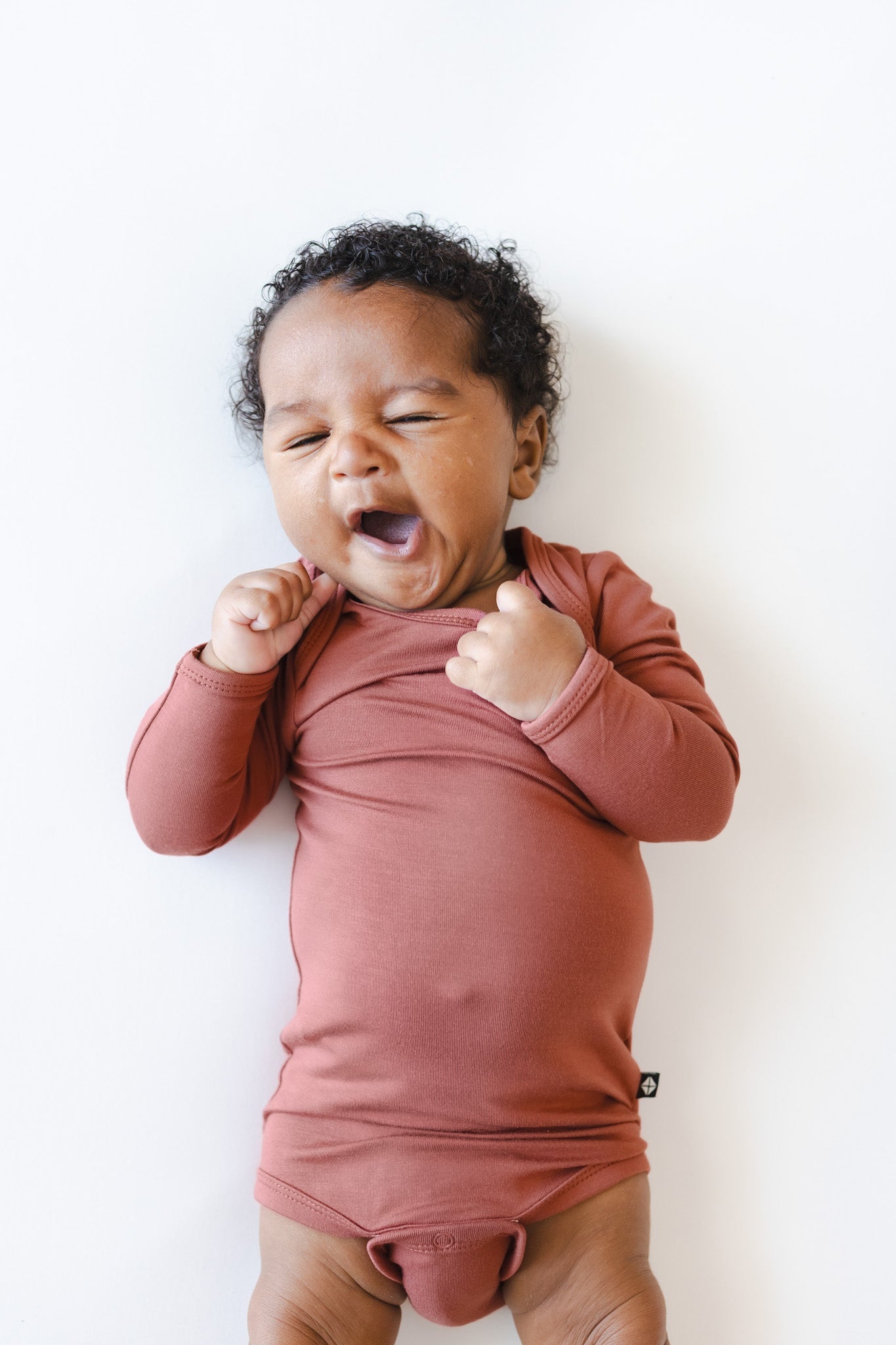 A baby wearing a dusty terracotta long-sleeve bodysuit, lying on their back against a clean white background.
