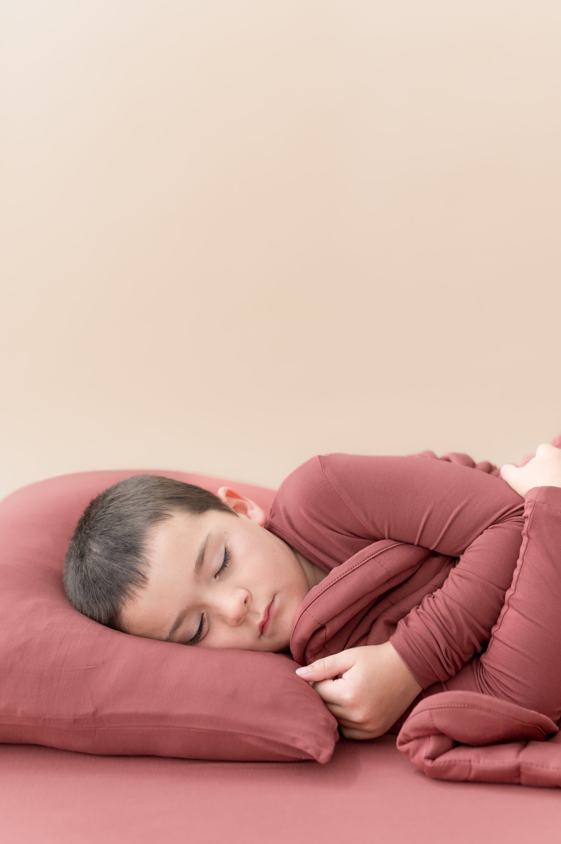 Boy sleeping on Standard Pillowcase in Ember covered under similar color blanket while wearing a similar color shirt