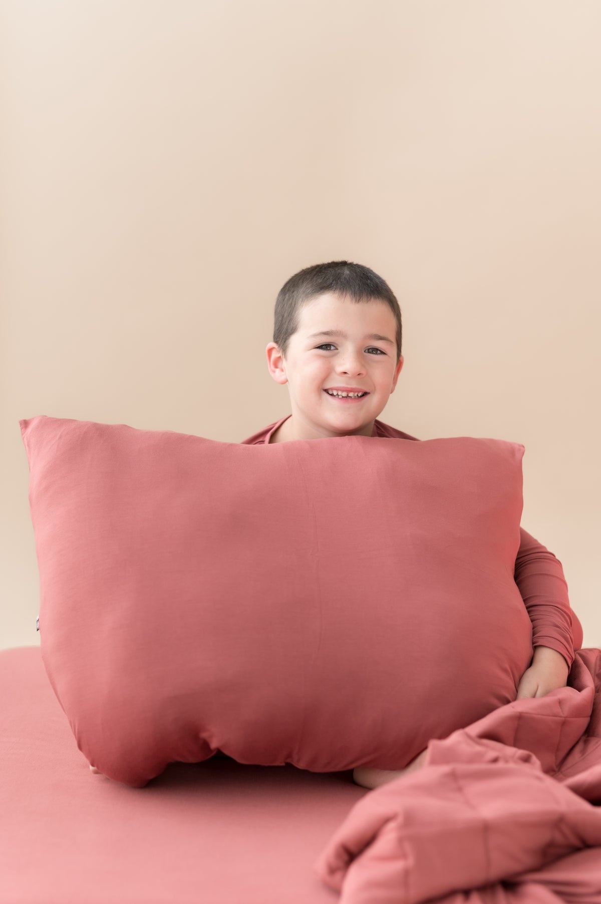 Boy sitting with Standard Pillowcase in Ember and similar color blanket and sheet