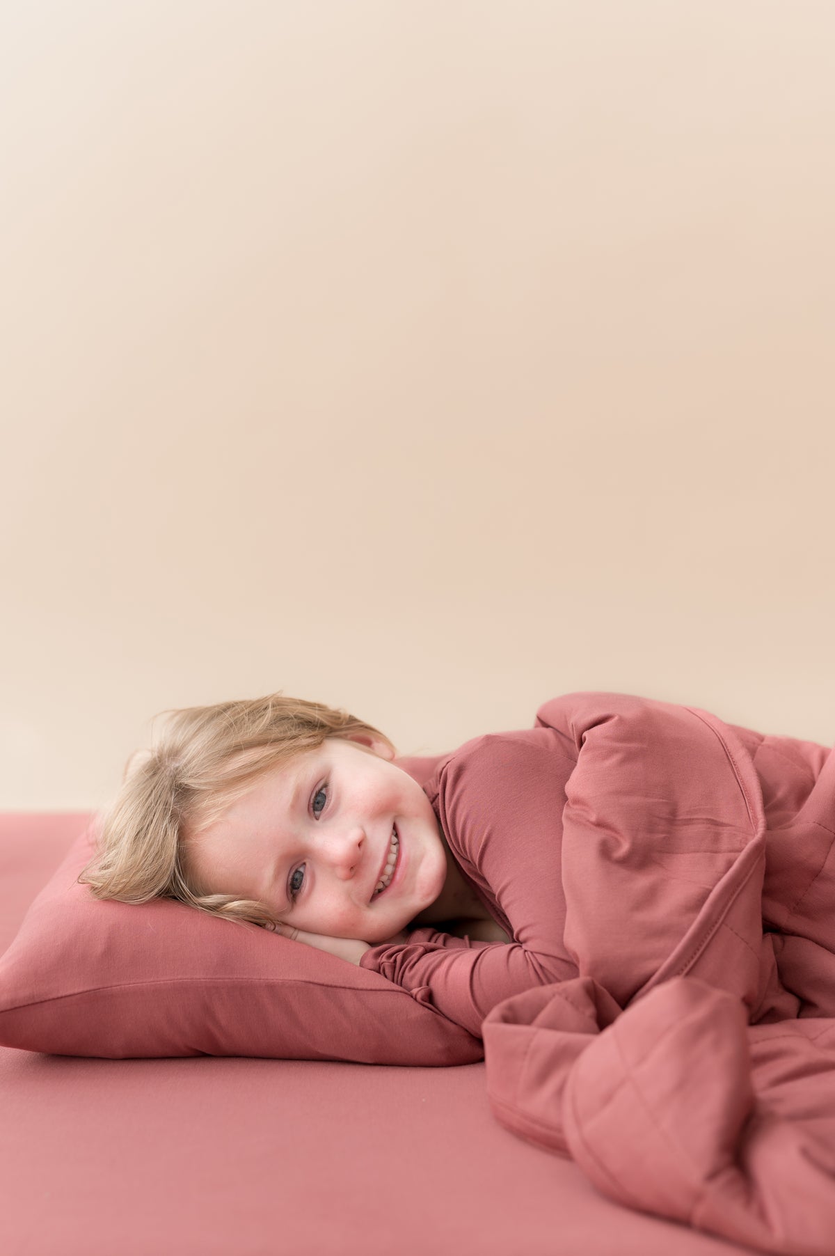 Boy lying on Toddler Pillowcase in Ember covered under similar color blanket and wearing ember shirt over ember sheets