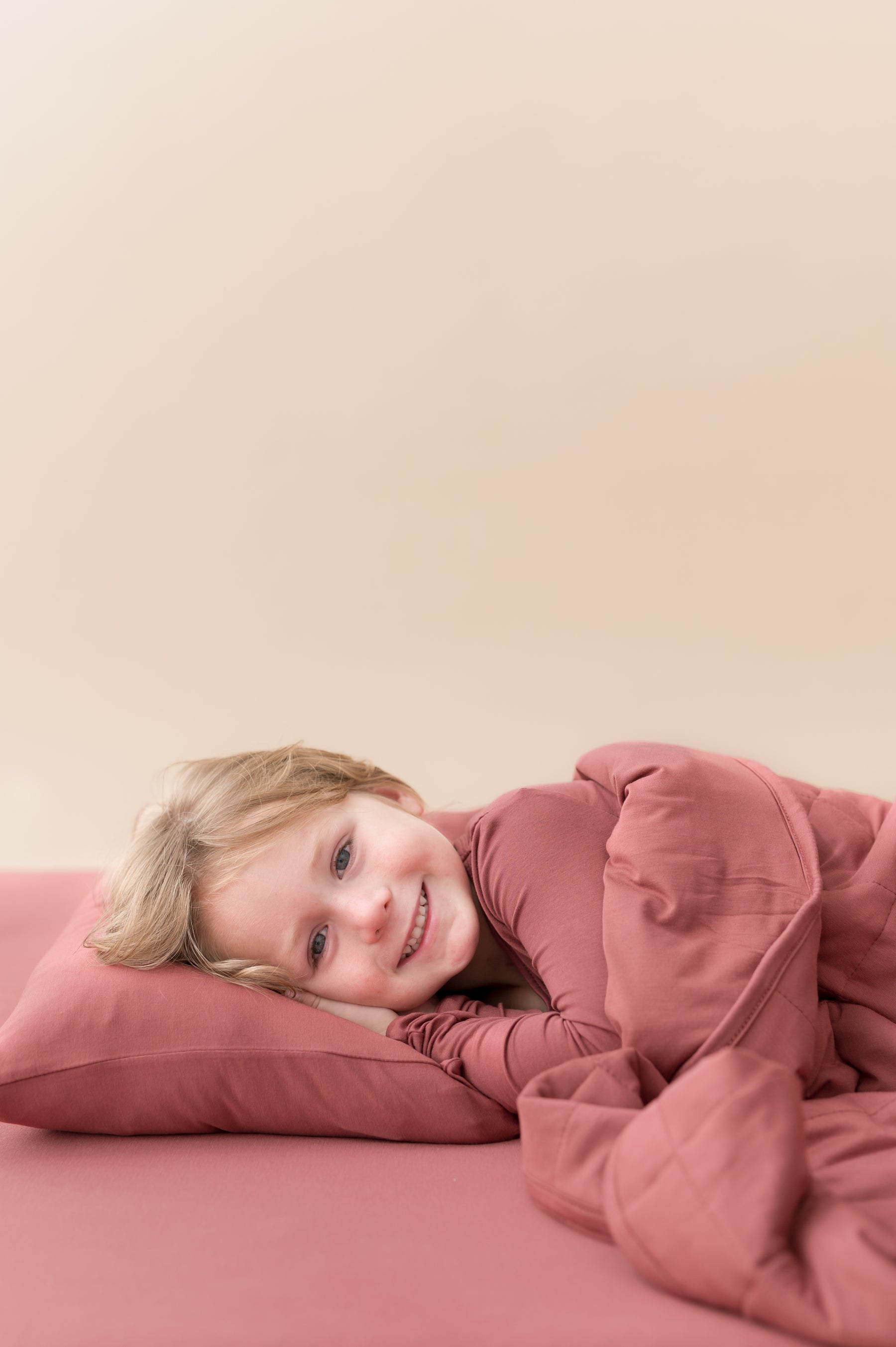 Boy lying on Toddler Pillowcase in Ember covered under similar color blanket and wearing ember shirt over ember sheets