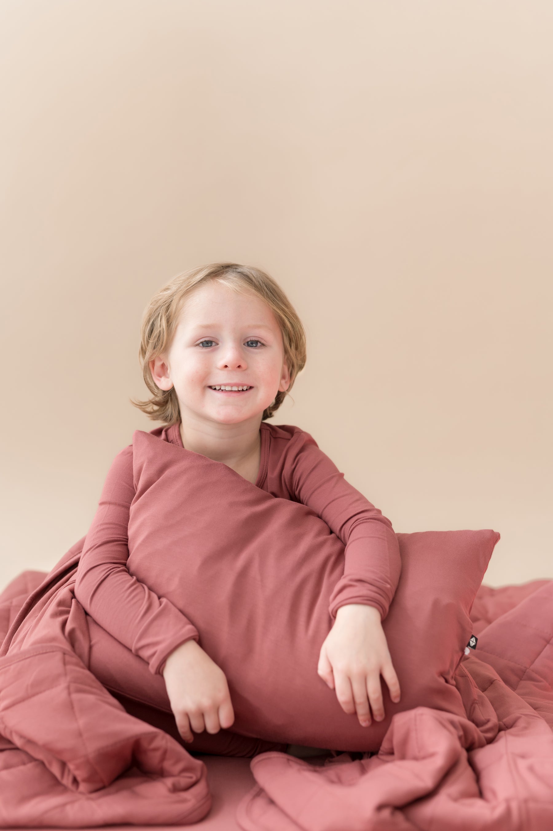 Boy holding Toddler Pillowcase in Ember while wearing a similar color shirt and blanket around him.