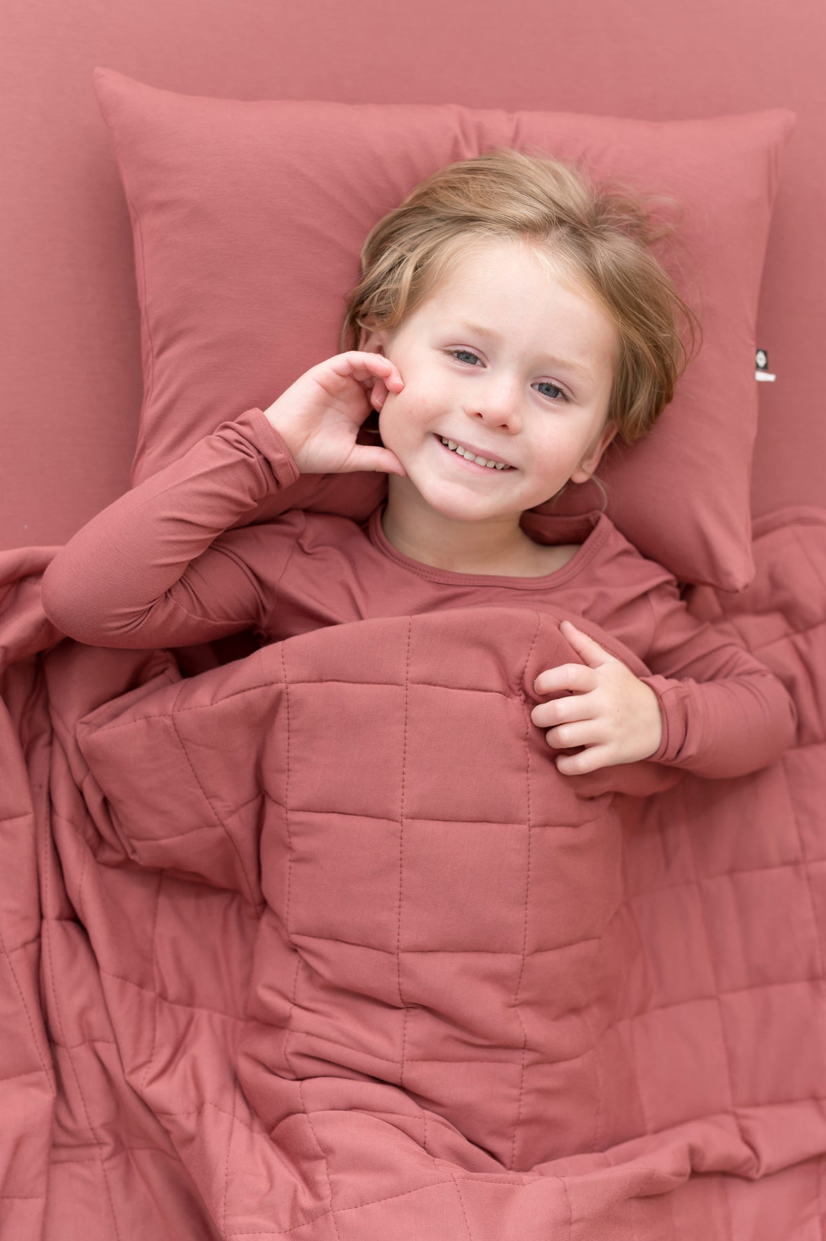 Child lying on Toddler Pillowcase in Ember while wearing a similar color shirt and blanket