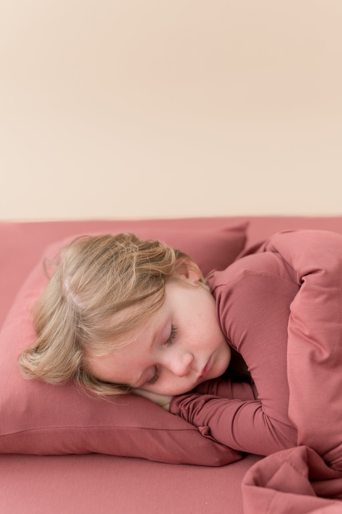 Child sleeping on Toddler Pillowcase in Ember on similar color sheets covered under Ember blanket and wearing ember shirt