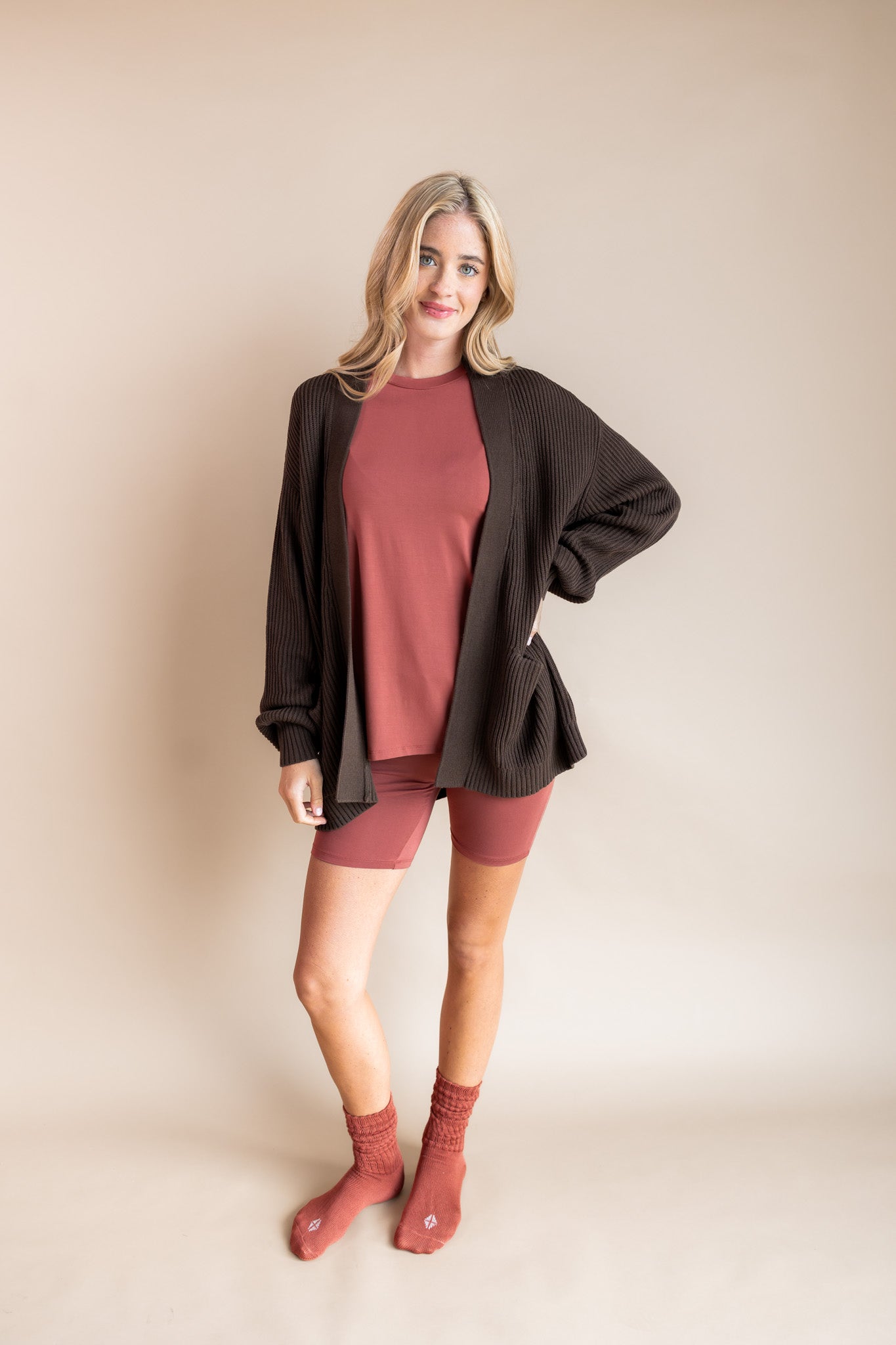 Modal wearing Biker short set in ember under chunky knit cardigan in espresso and adult socks in ember on a beige background