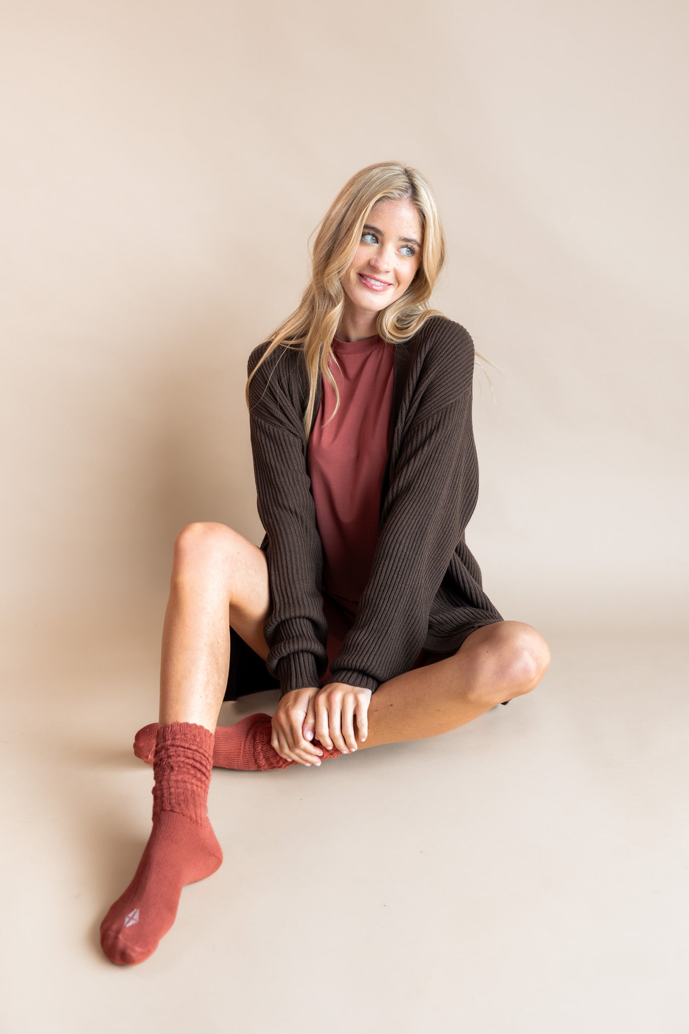 Modal wearing Biker short set in ember under chunky knit cardigan in espresso and adult socks in ember on a beige background