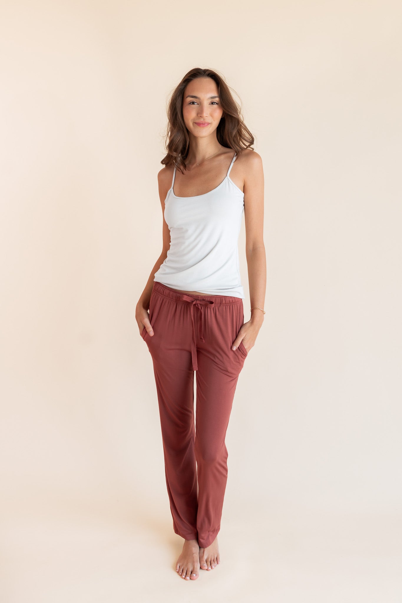 Model wearing Women's Lounge Pants in Ember under white camisole on a beige background