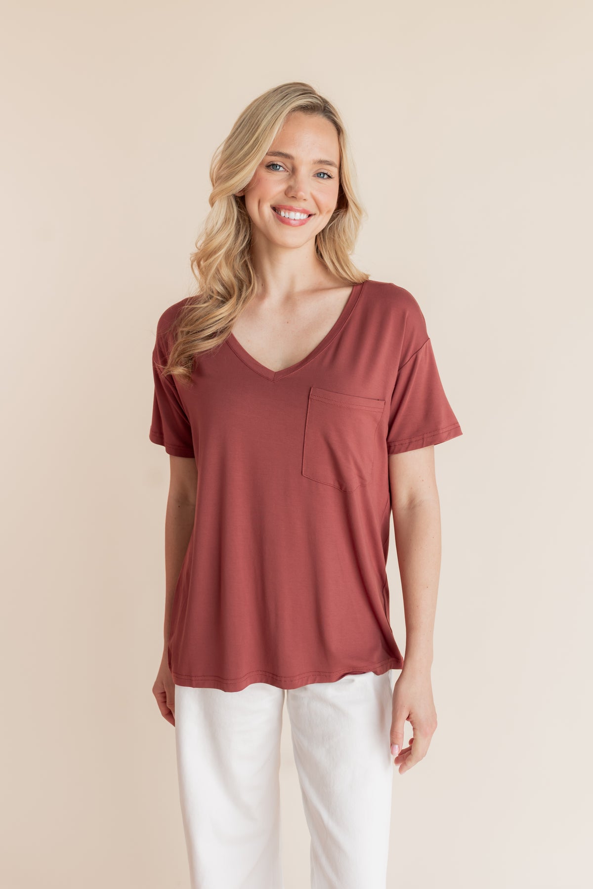 Model wearing Women's Oversized V-Neck Tee in Ember over white pants on a beige background