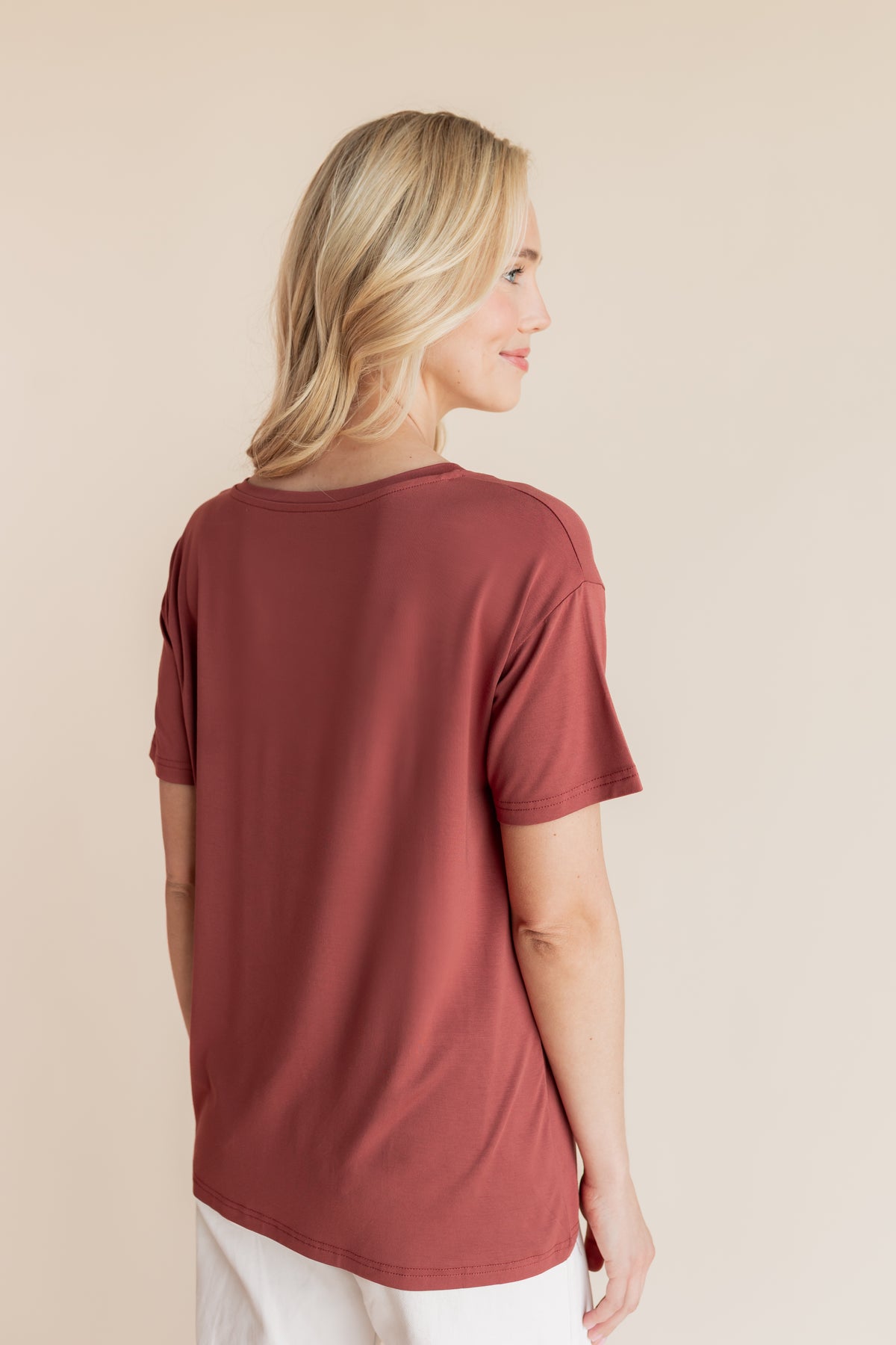 Model showcasing backside of Women's Oversized V-Neck Tee in Ember over white pants on a beige background