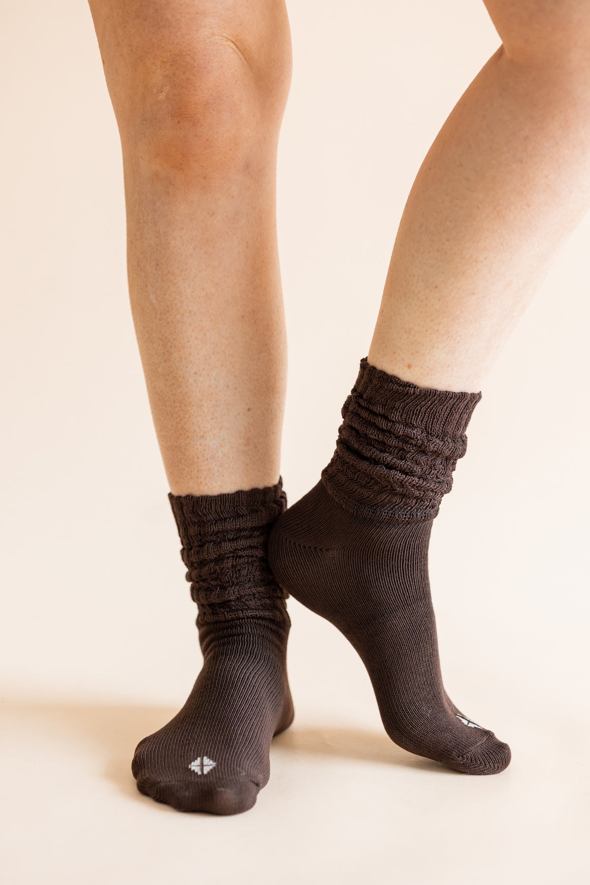 A close-up of a person's legs wearing dark brown ribbed crew socks against a solid light beige background.