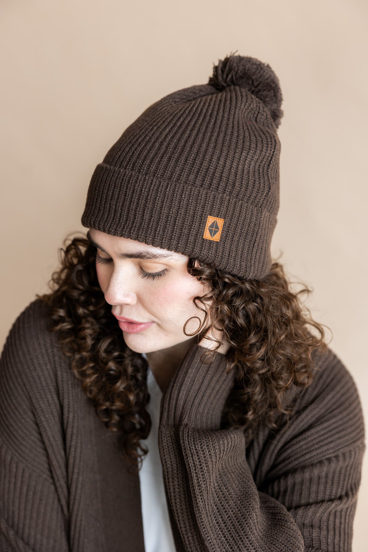 Modal posing in Chunky Knit Adult Pom in Espresso over Chunky knit Cardigan in espresso on a beige background