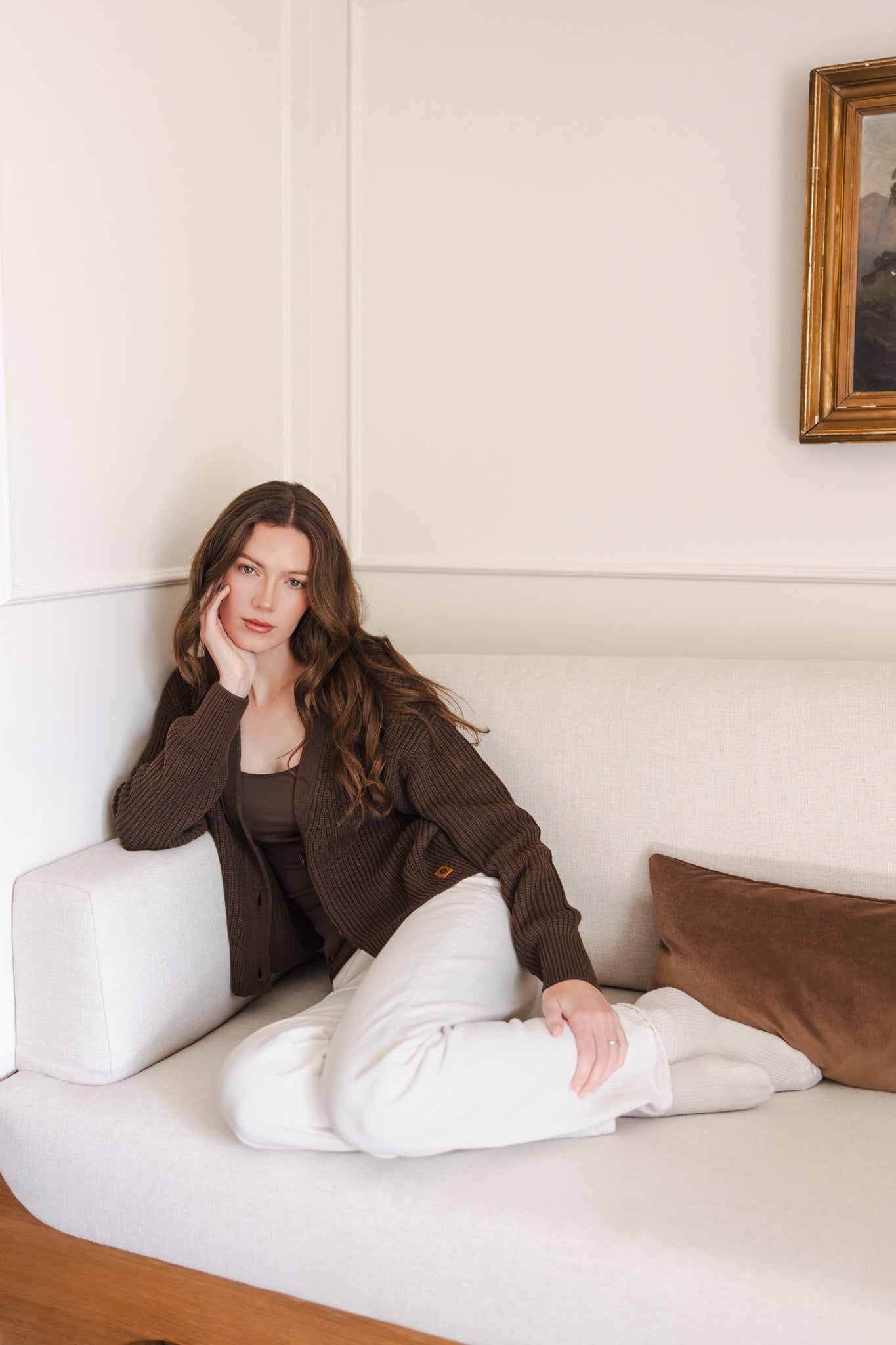 Modal sitting on a white sofa wearing Chunky Knit Women's Cropped Cardigan in Espresso over white pants