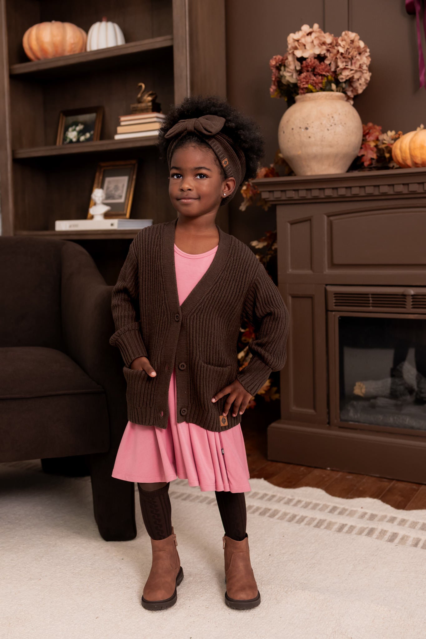 Girl wearing Chunky Knit Bow Headband in Espresso over Pink twirl dress and chunky knit oversized cardigan in espresso standing in a living room