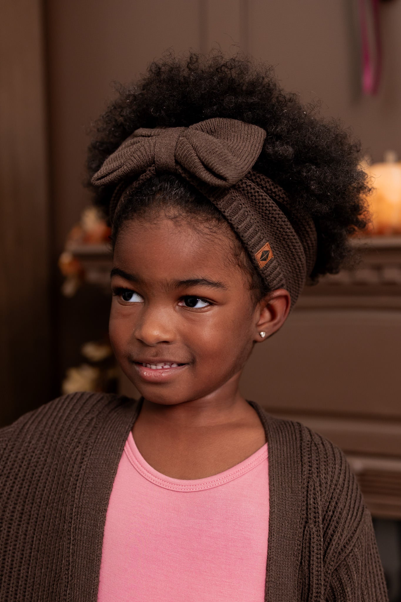 Girl wearing Chunky Knit Bow Headband in Espresso over Pink T-shir and chunky knit oversized cardigan in espresso