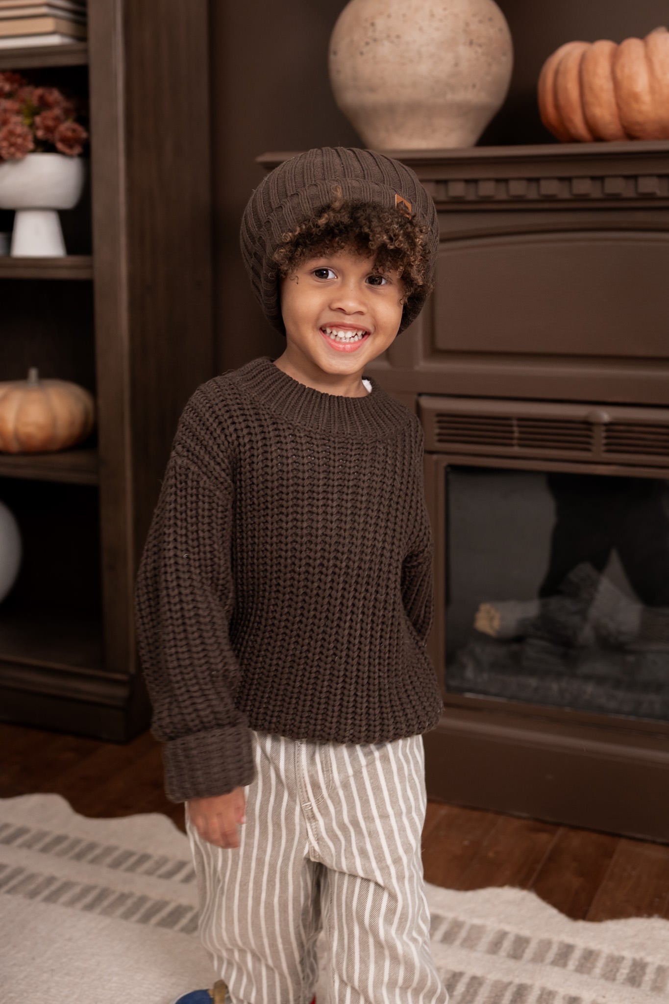 Boy wearing Chunky Knit Sweater and chunky knit ribbed beanie in espresso over pants standing in a living room